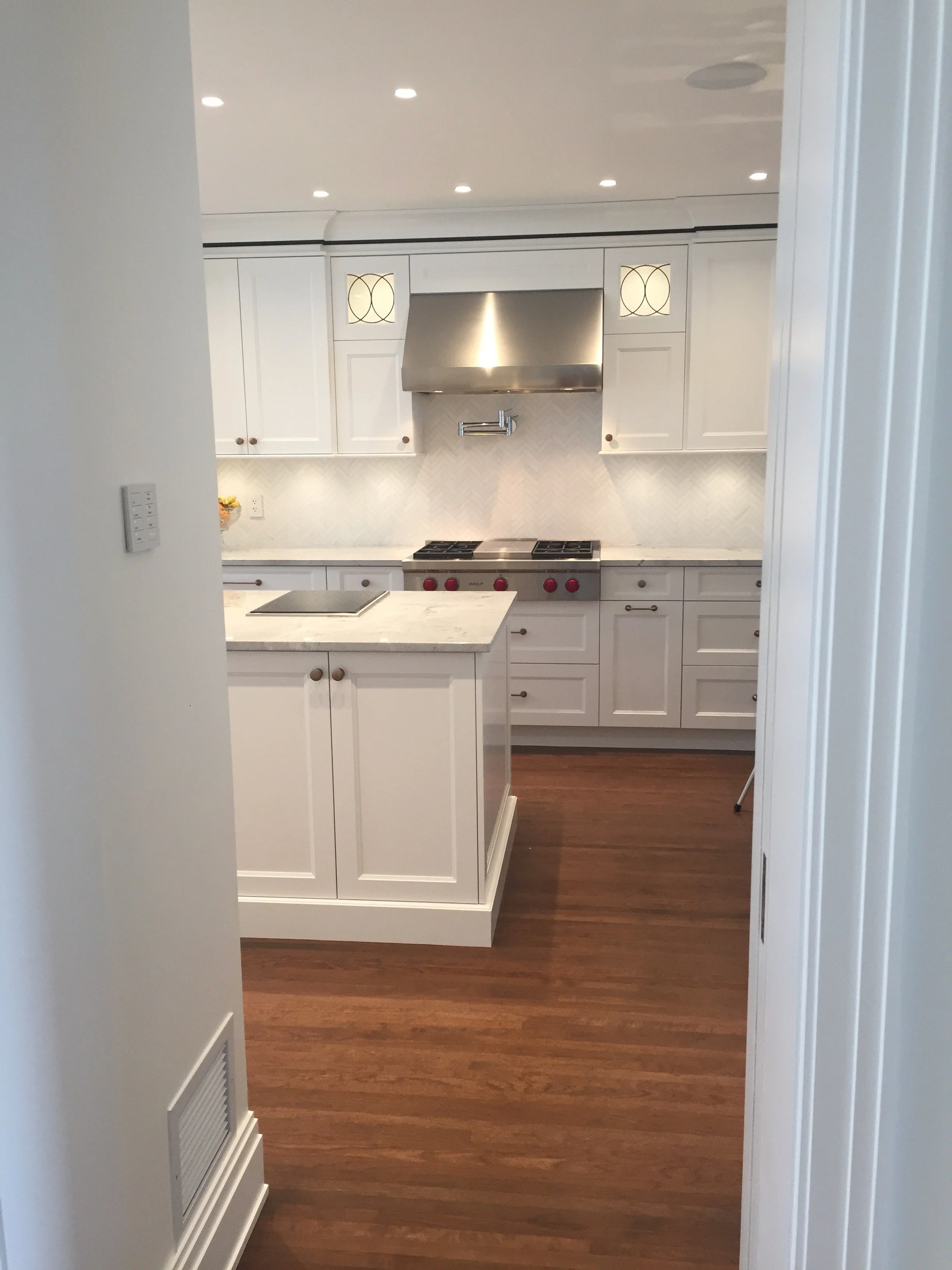A modern kitchen with white cabinets, a marble island, a stainless steel range hood, and hardwood floors.