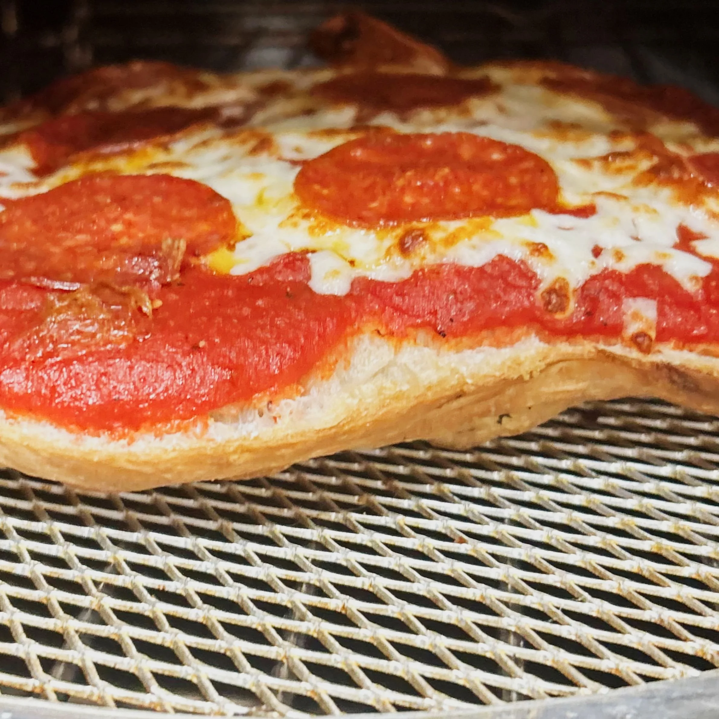 Close-up of a pepperoni pizza with melted cheese on a metal cooling rack.