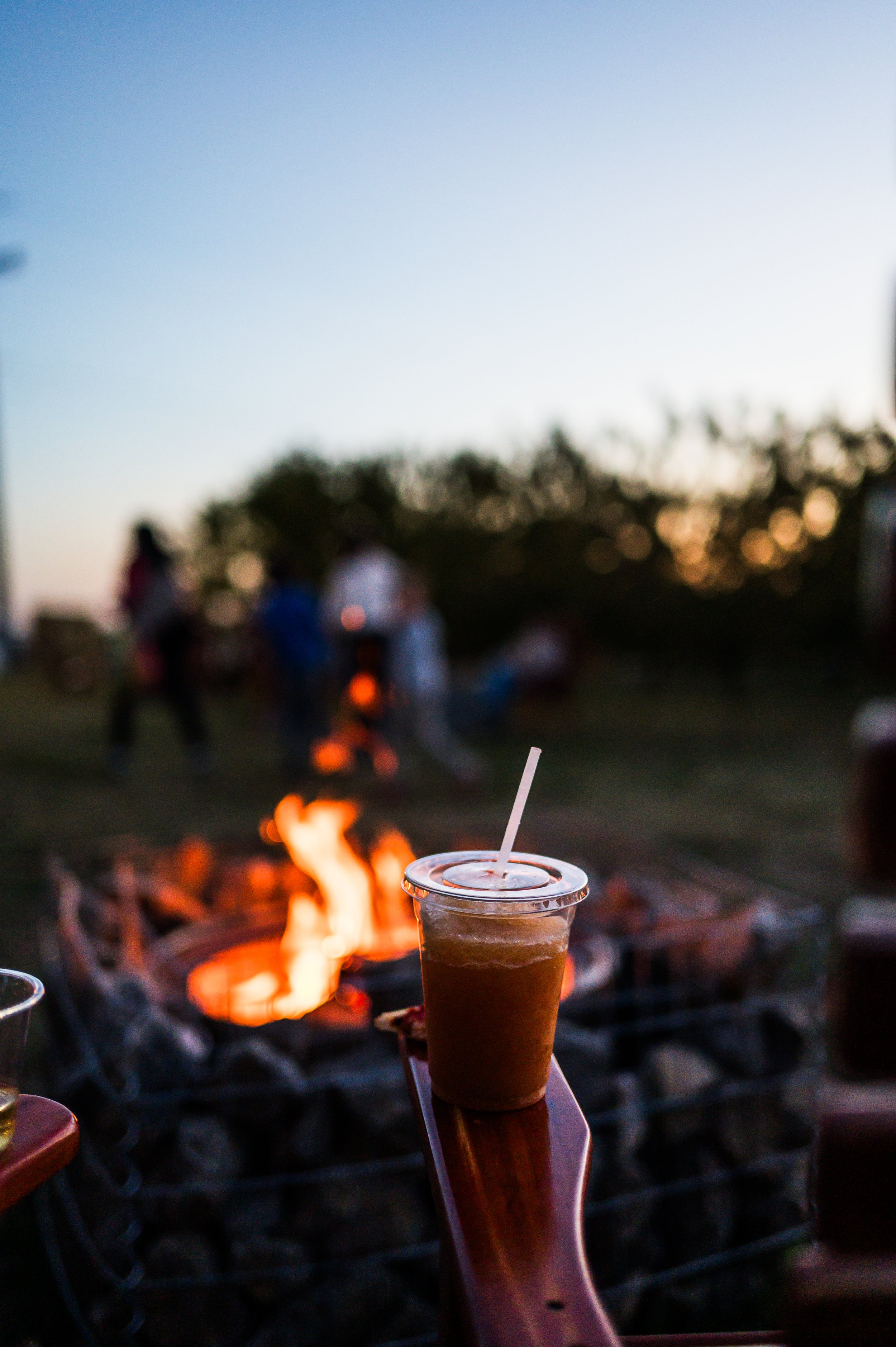 A smiling woman with natural curly hair, wearing glasses, earrings, a striped shirt, and layered necklaces, sitting in an indoor setting.