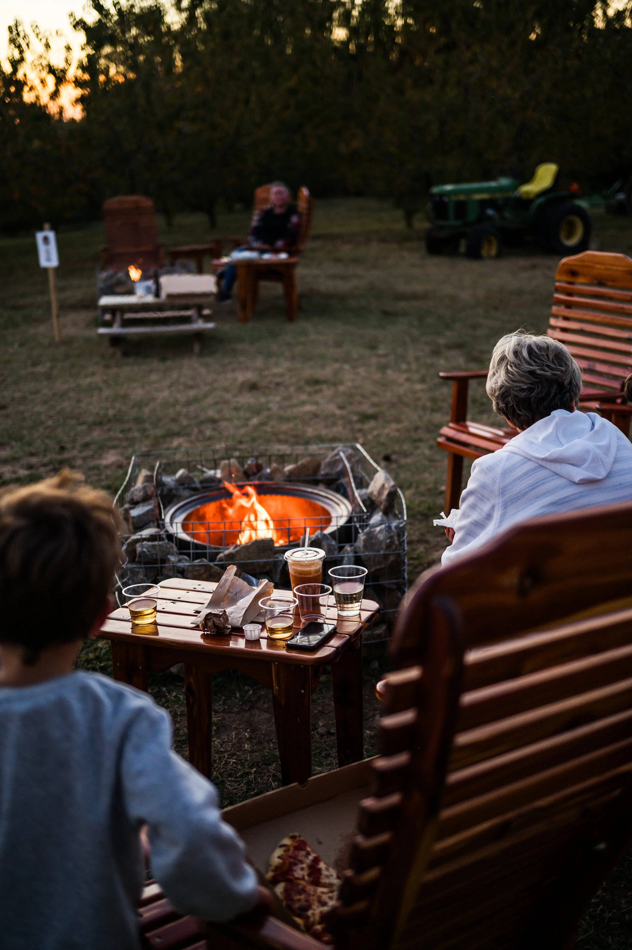 A man with curly dark hair, glasses, and a beard, wearing a dark green sweater, looking slightly to the side with a neutral expression, against a plain background with a plant in the distance.