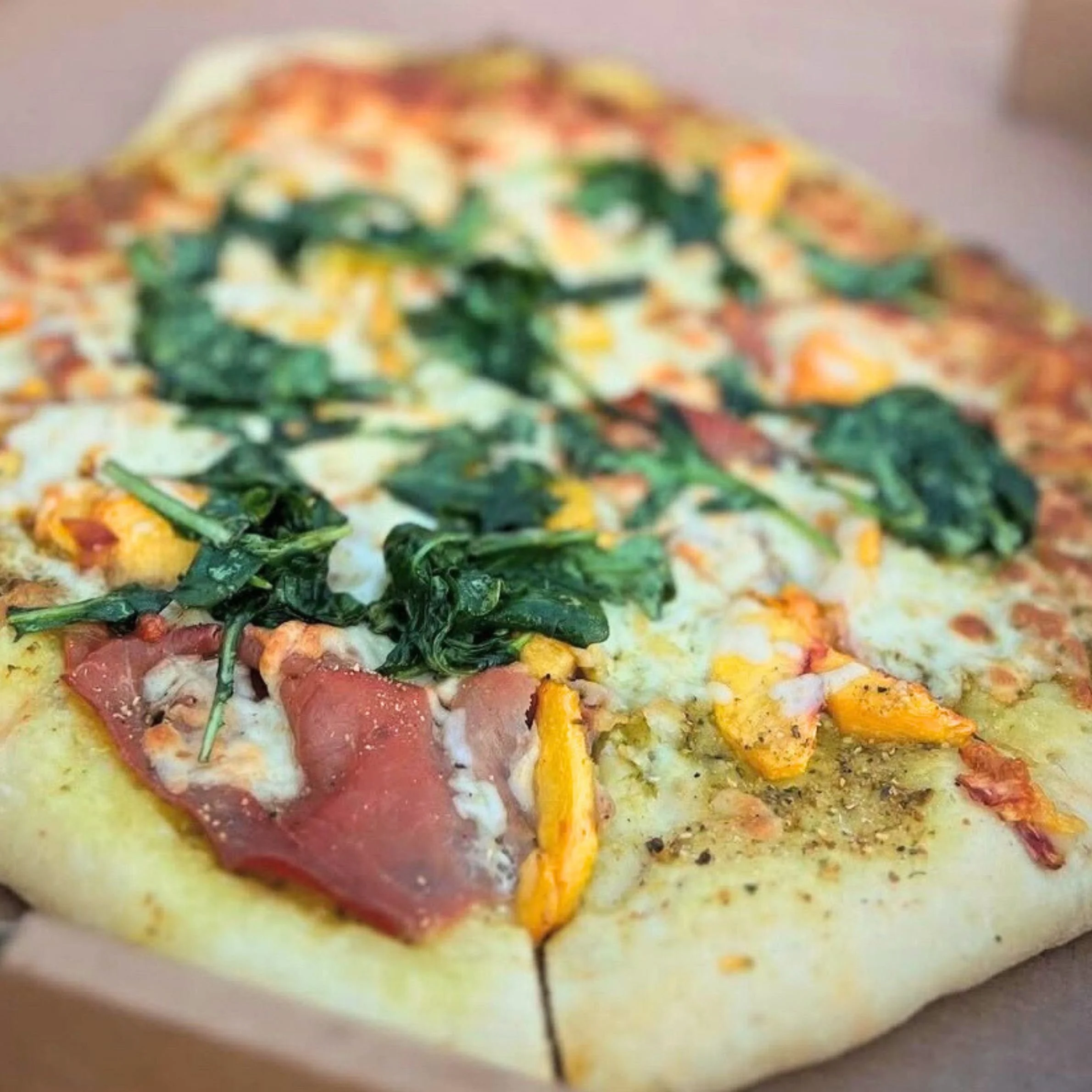 Close-up of a pizza with spinach, cheese, ham, and yellow bell peppers.