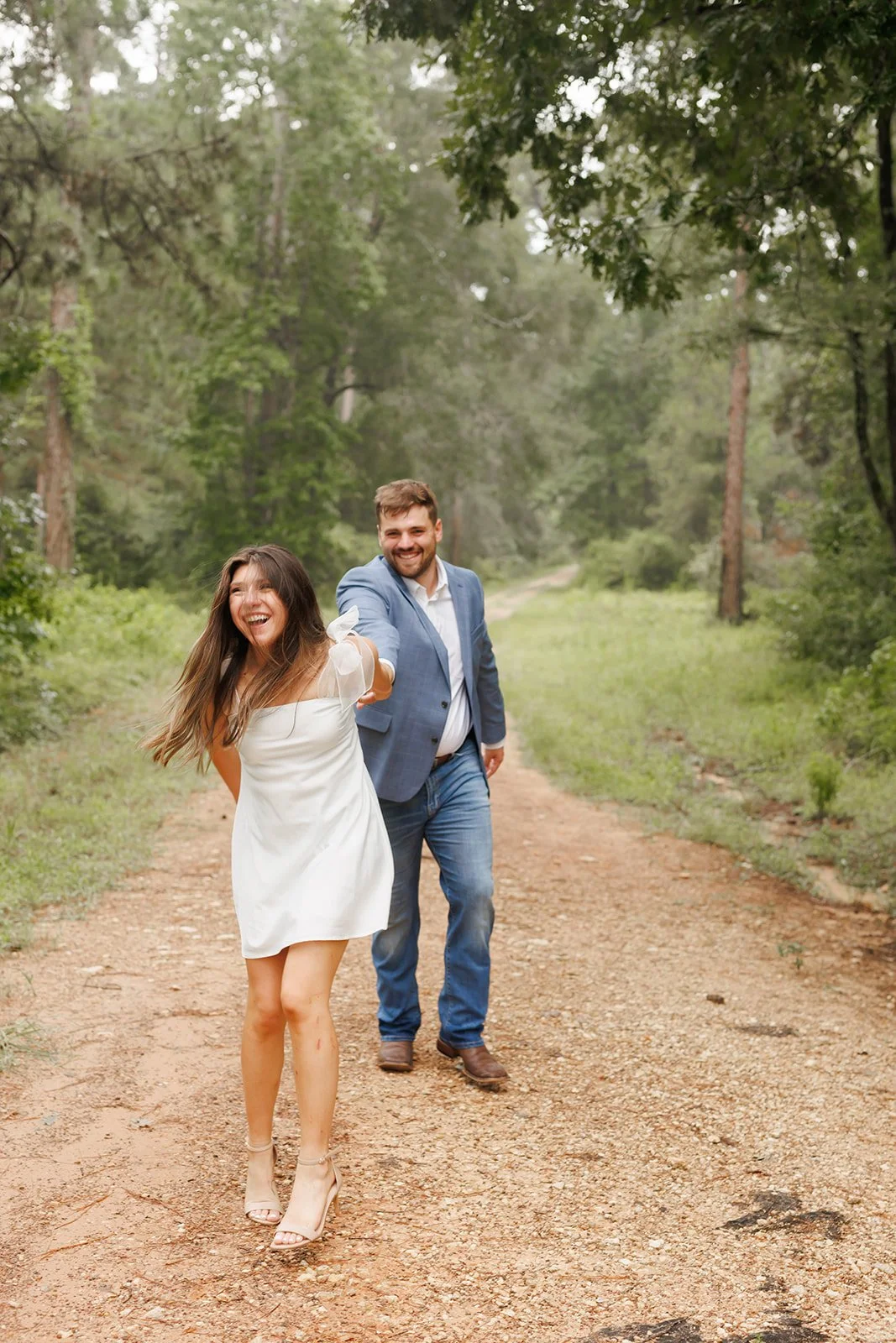 Romantic forest engagement session in The Woodlands at WG jones state park as a couple walks hand-in-hand along a dirt trail — photographed by Wild Ivy Creative.