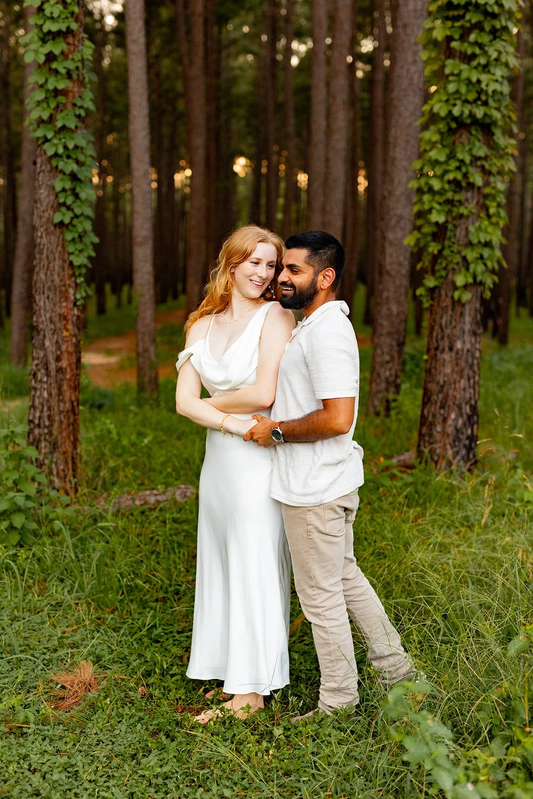 Casual and romantic engagement photo of a couple sitting on grass in a Houston-area forest clearing — photographed by Wild Ivy Creative.