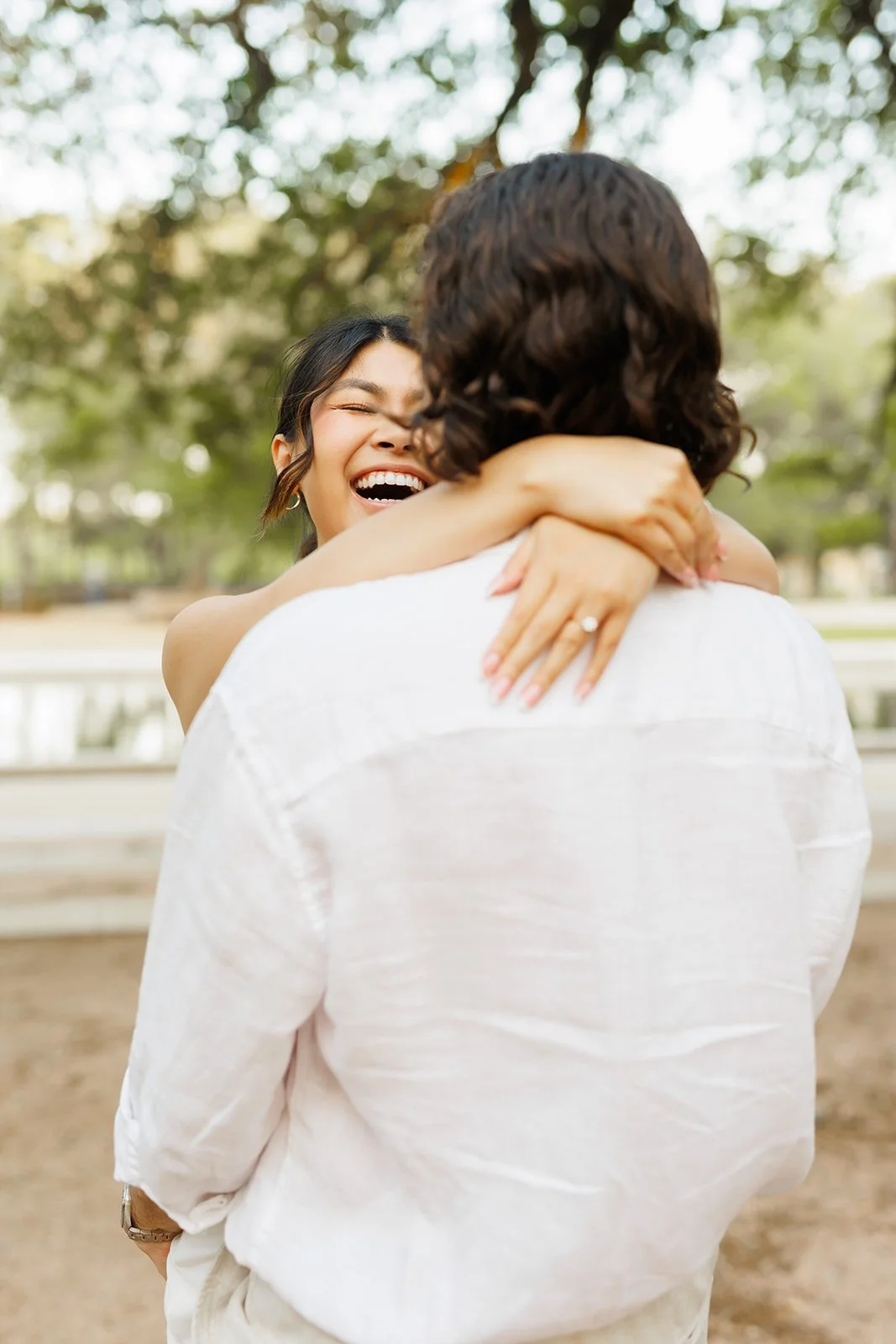 Playful outdoor moment of a woman hugging her partner from behind, surrounded by trees during a candid engagement session with Wild Ivy Creative Photography.