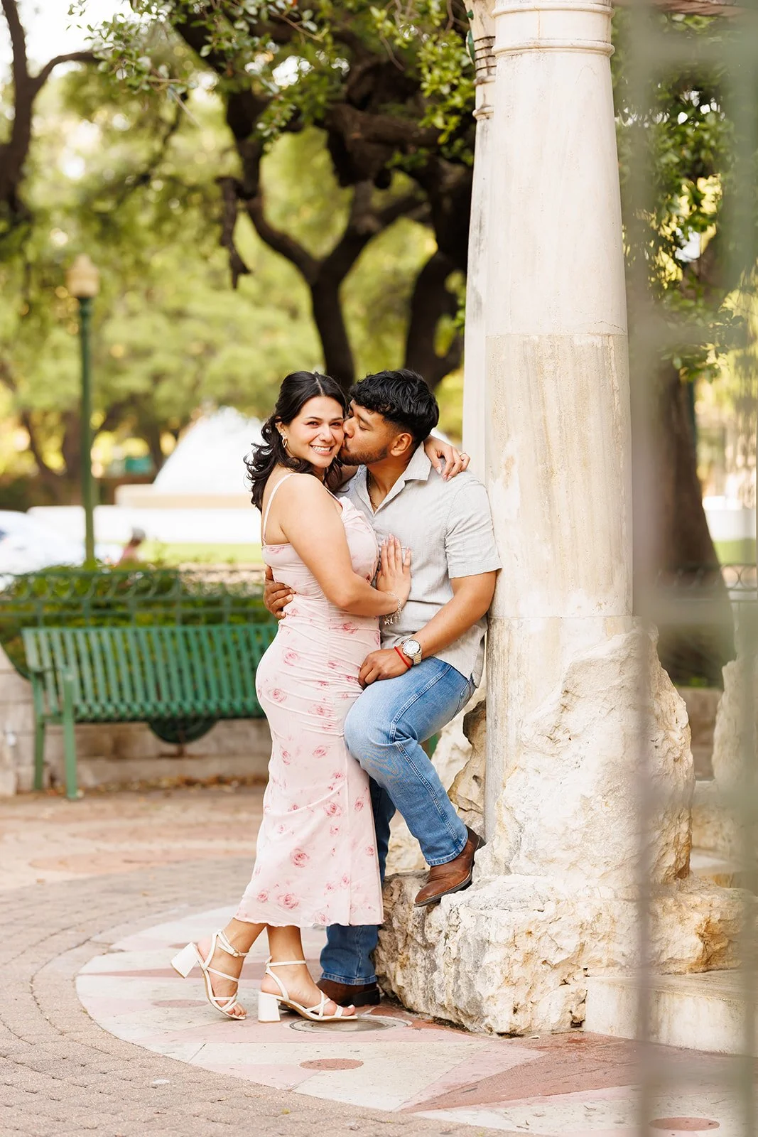 Natural park engagement session in The Woodlands — couple kissing beside a stone column with greenery all around — Wild Ivy Creative.