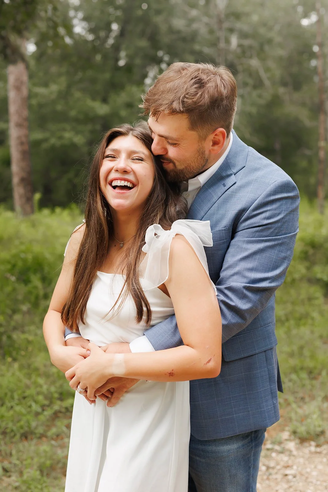 Playful outdoor engagement moment with a couple touching noses and smiling beneath a canopy of trees in The Woodlands — Wild Ivy Creative.