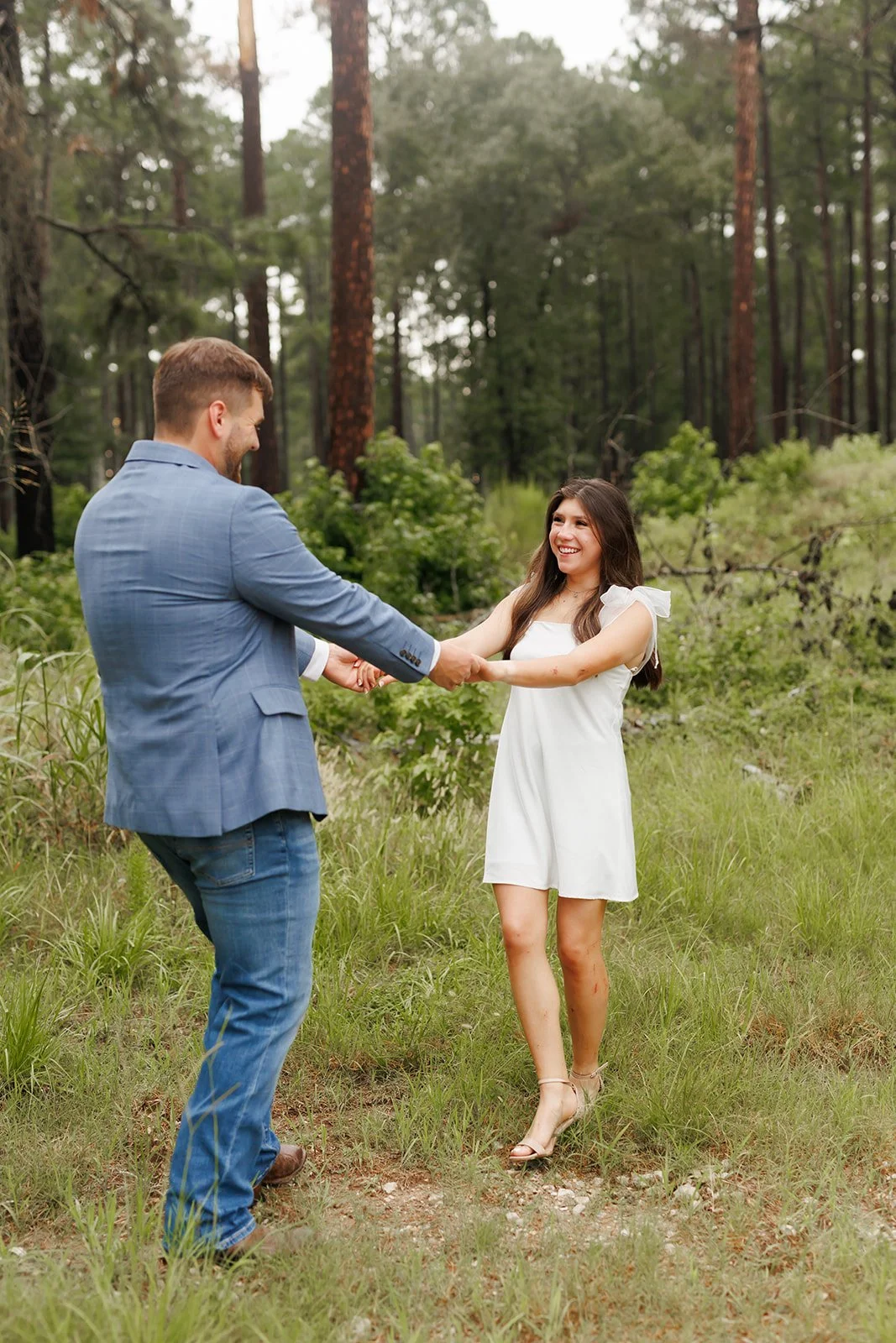 Joyful forest engagement session with a couple holding hands and smiling, featuring modern outfits in a wooded in WG Jones State Park in the Woodlands.