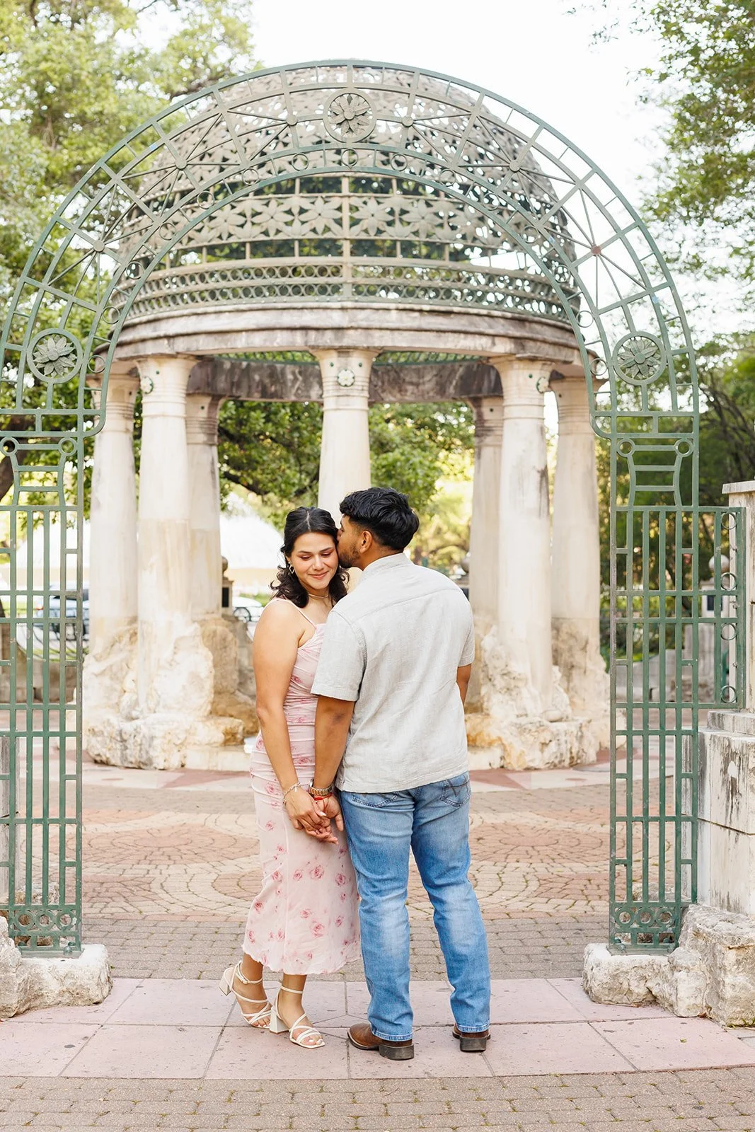 Romantic Houston park engagement photo with a couple kissing under a decorative archway and stone pavilion — Wild Ivy Creative.