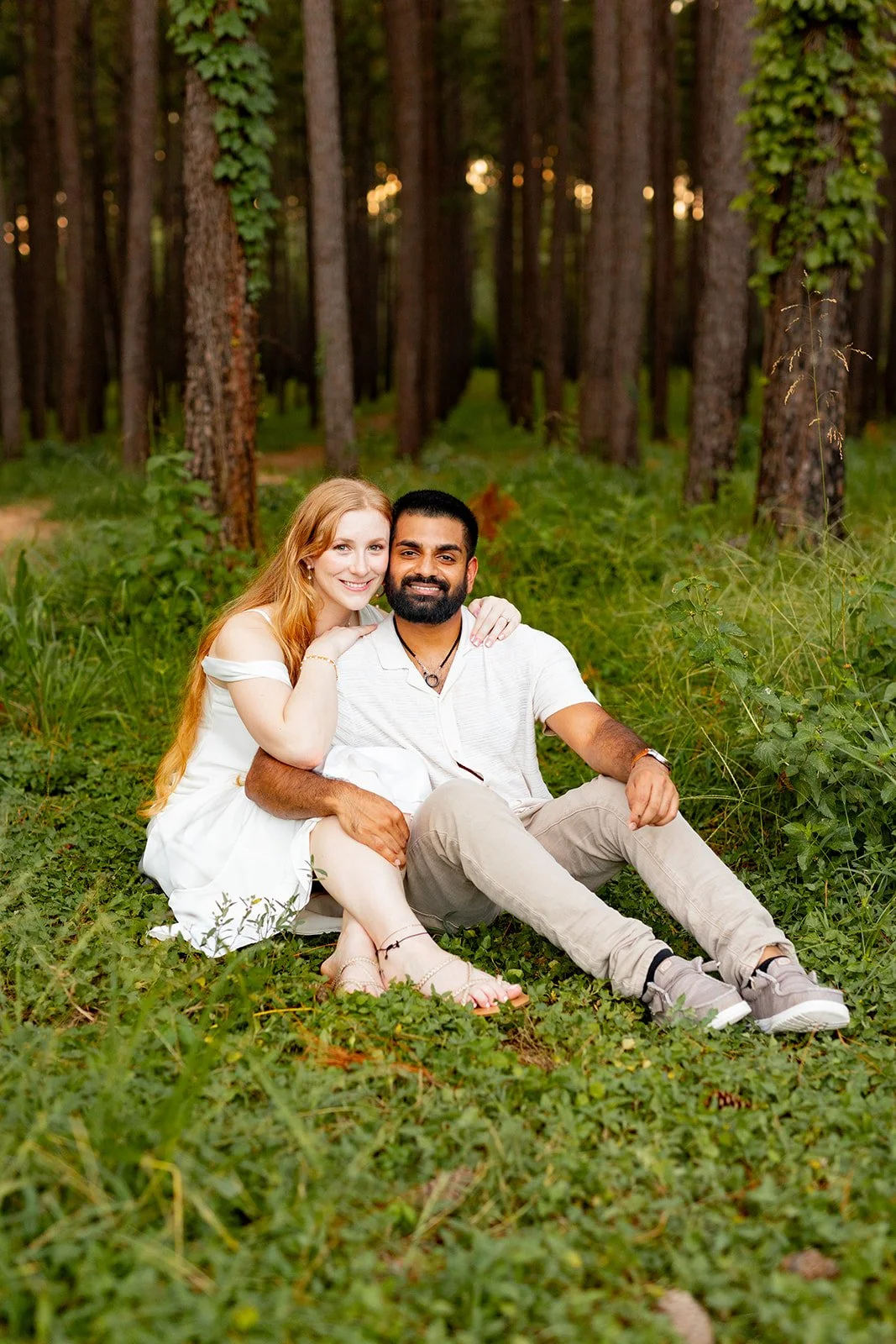 Casual and romantic engagement photo of a couple sitting on grass in a Houston-area forest clearing at WG Jones — photographed by Wild Ivy Creative.