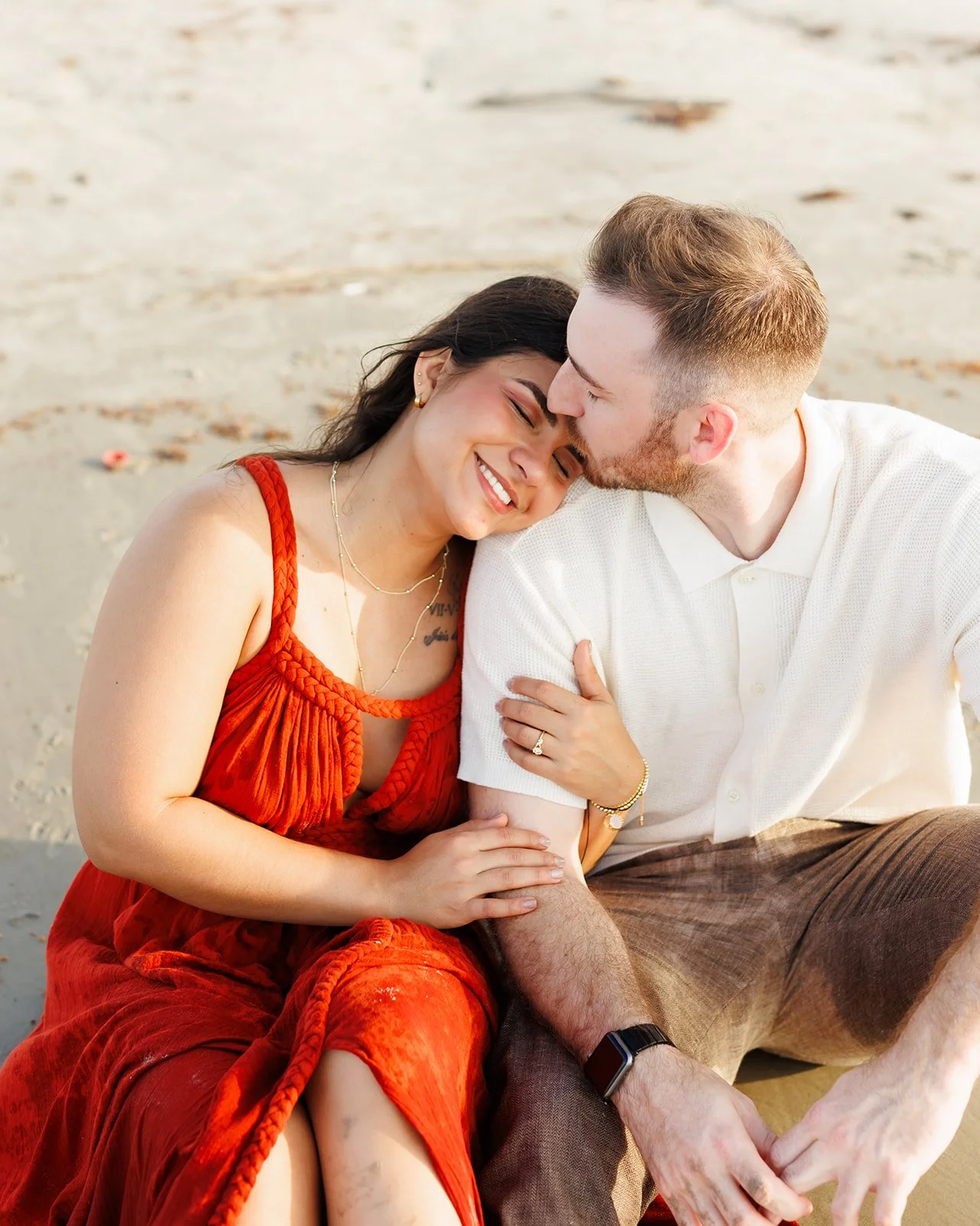 Tender Galveston beach engagement photo — man kissing his partner’s forehead as they sit in the sand — Wild Ivy Creative.