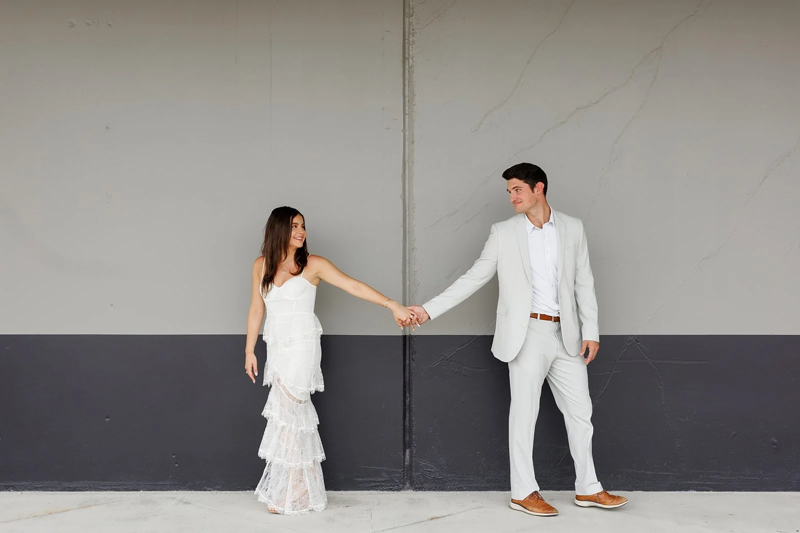 Minimalist Houston engagement portrait with a couple in matching white outfits smiling at each other against a modern gray backdrop — Wild Ivy Creative.