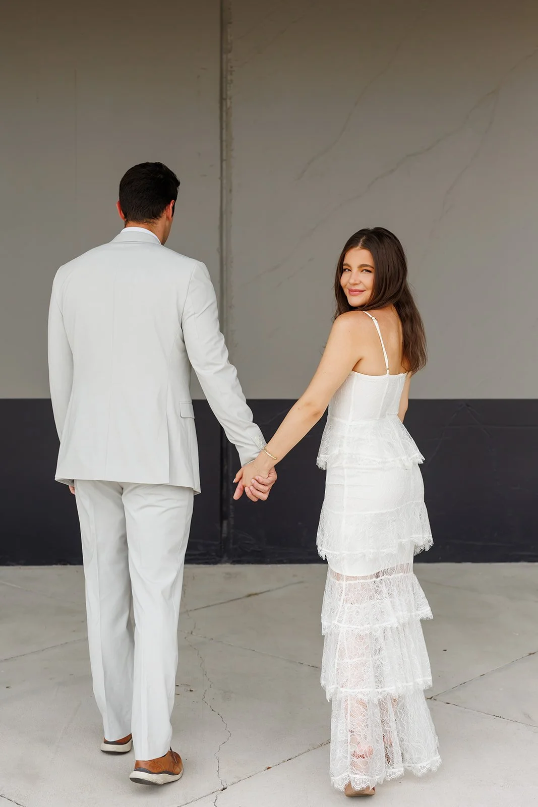 A couple dressed in white holding hands, with the woman looking at the camera and smiling.