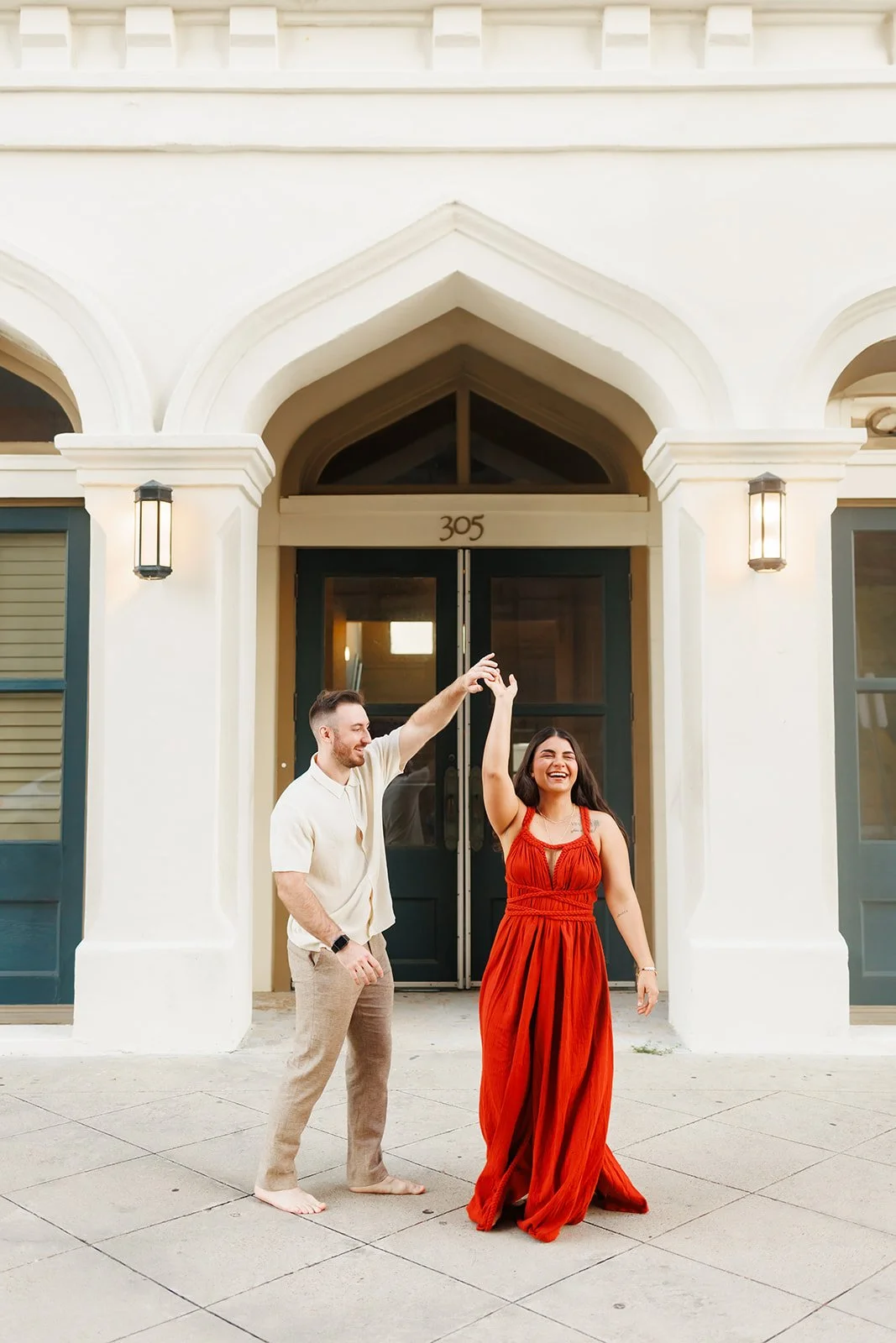 Joyful Downtown Galveston engagement session in front of a home numbered 305 — couple dancing and laughing in colorful outfits — Wild Ivy Creative.