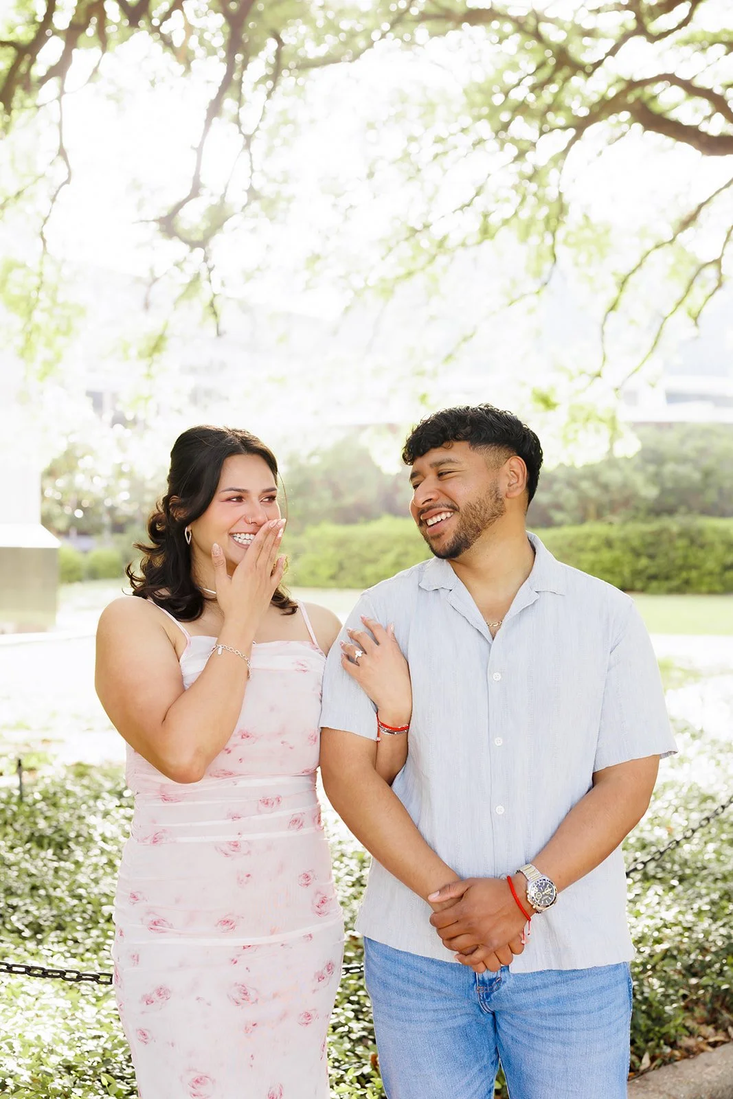 Playful outdoor engagement photo under a tree in Houston in the Museum District after a surprise Proposal — couple laughing with the woman covering her mouth, by Wild Ivy Creative.