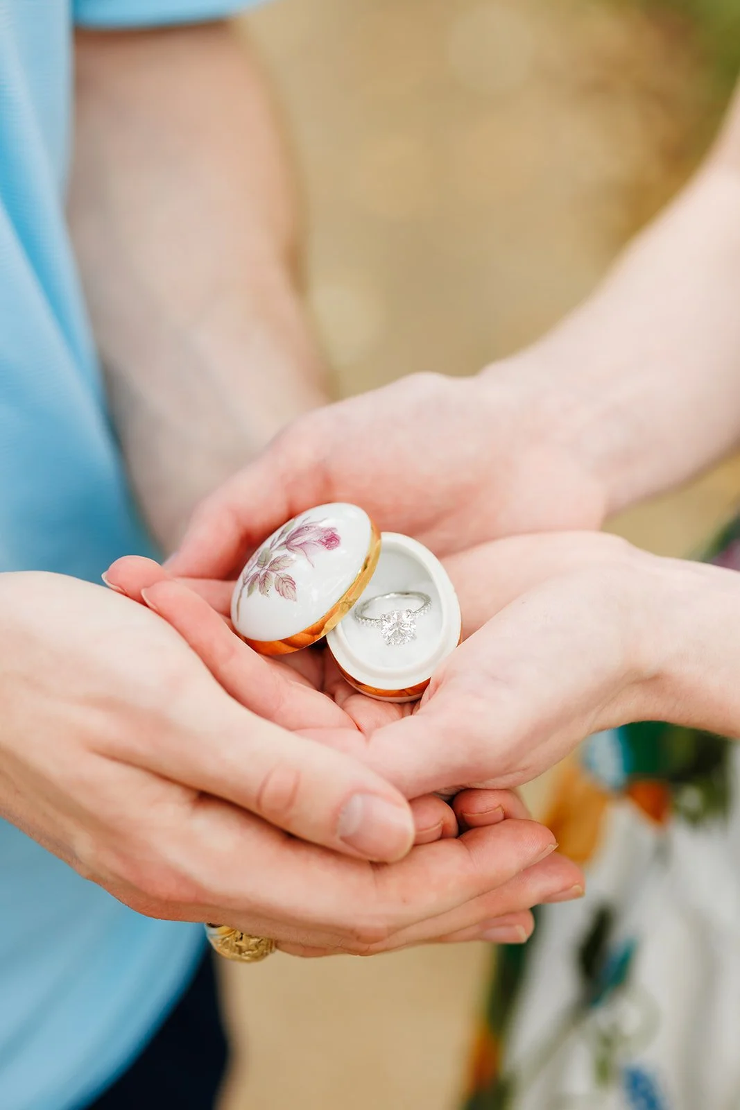 Hands holding a jewelry box with a diamond ring inside.