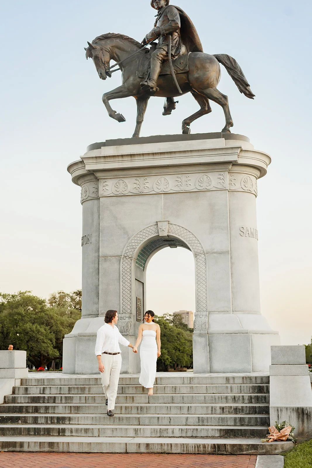 Houston engagement photo of a couple walking down stone monument steps below a historic equestrian statue — Wild Ivy Creative.