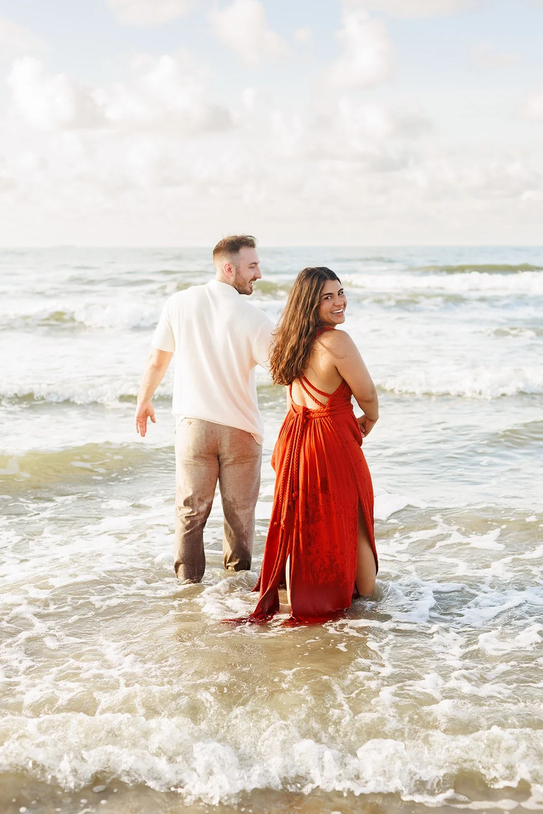 Joyful Galveston engagement photo — couple laughing and standing in the surf, dressed in bright coastal tones — Wild Ivy Creative.
