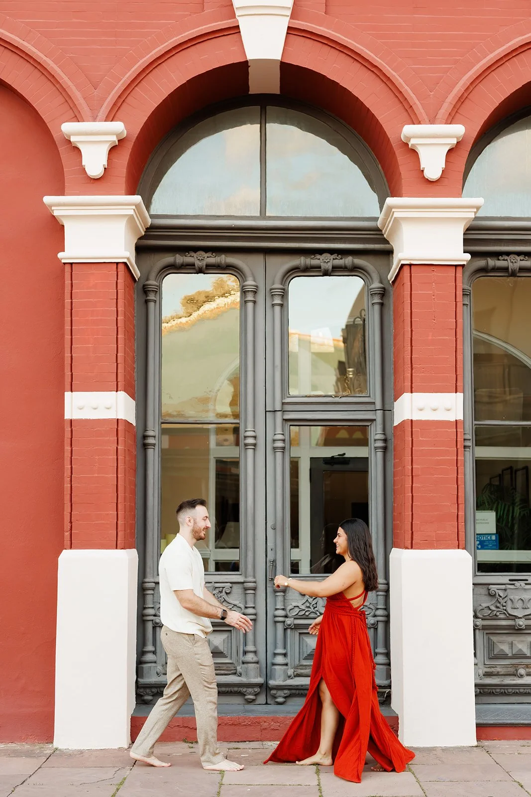 Elegant Houston engagement photo of a couple dancing in front of a red brick building with ornate windows and a grand gray door — Wild Ivy Creative.