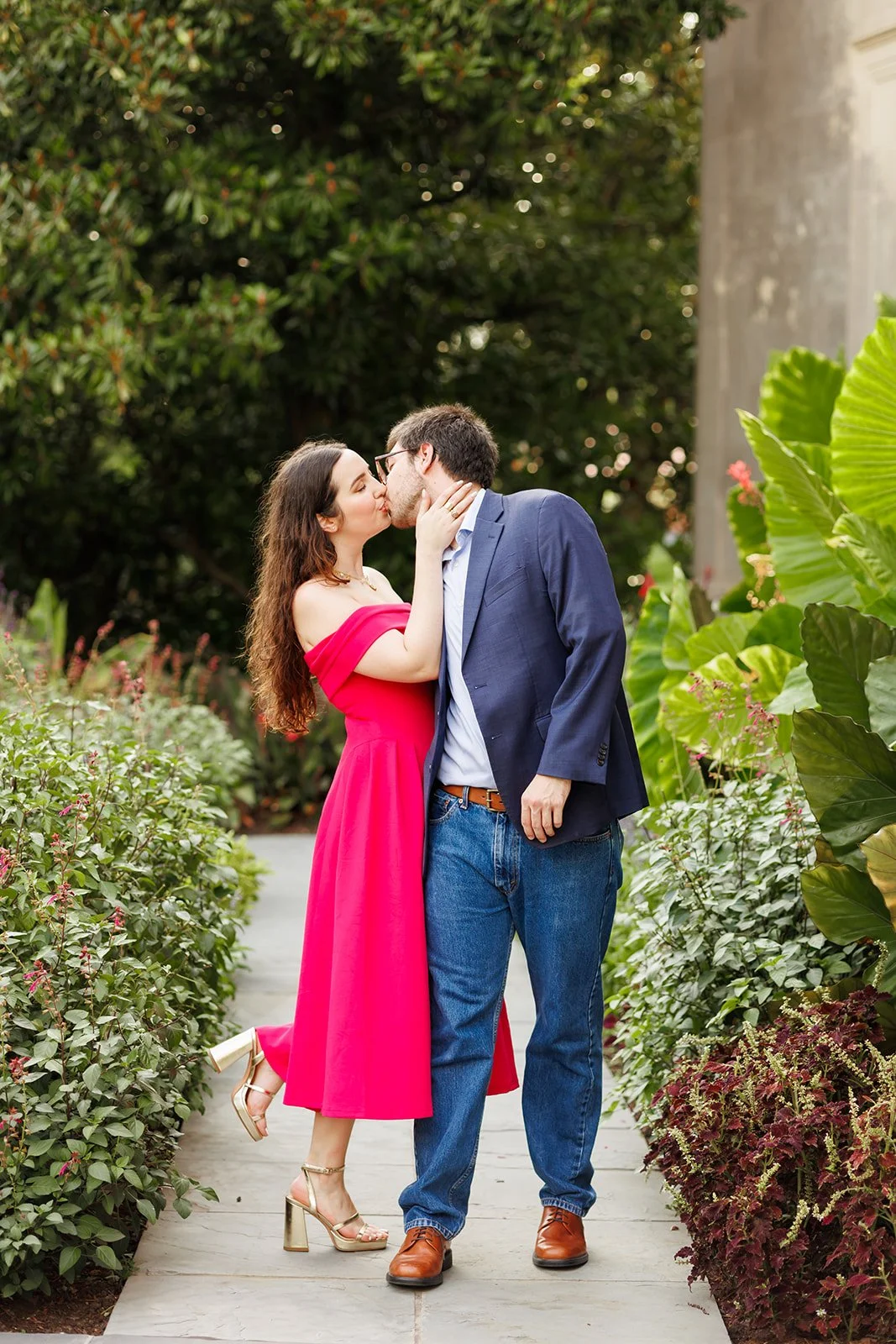 A couple sharing a kiss on a walkway surrounded by lush green plants