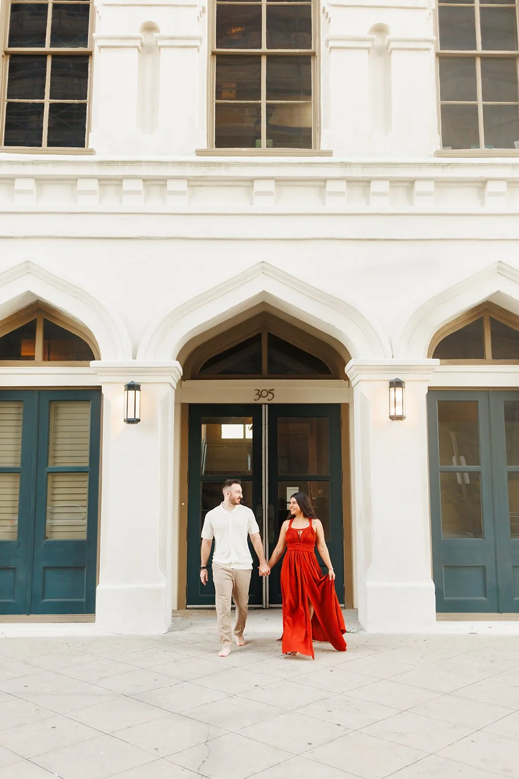 Elegant outdoor engagement photo with a couple in front of a white building with arched green doors in Downtown Galveston — photographed by Wild Ivy Creative.