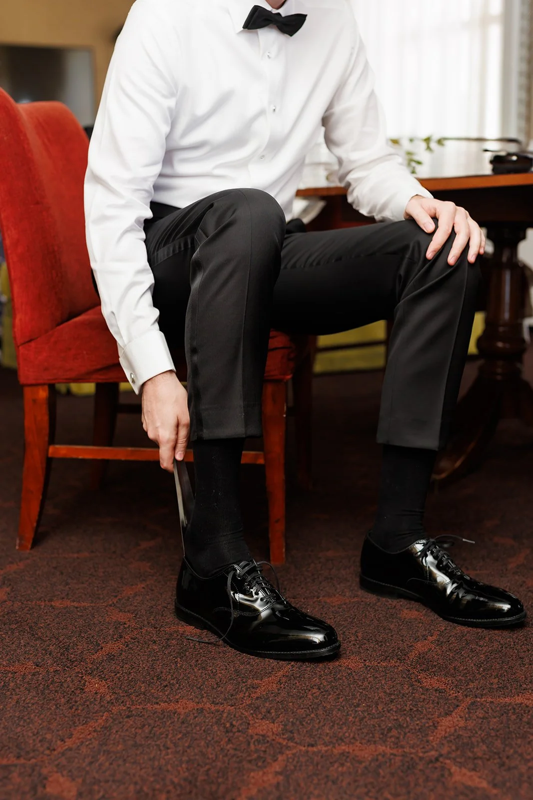 Groom putting shoes on in luxury hotel suite captured by Houston wedding photographer - Wild Ivy Creative Photography