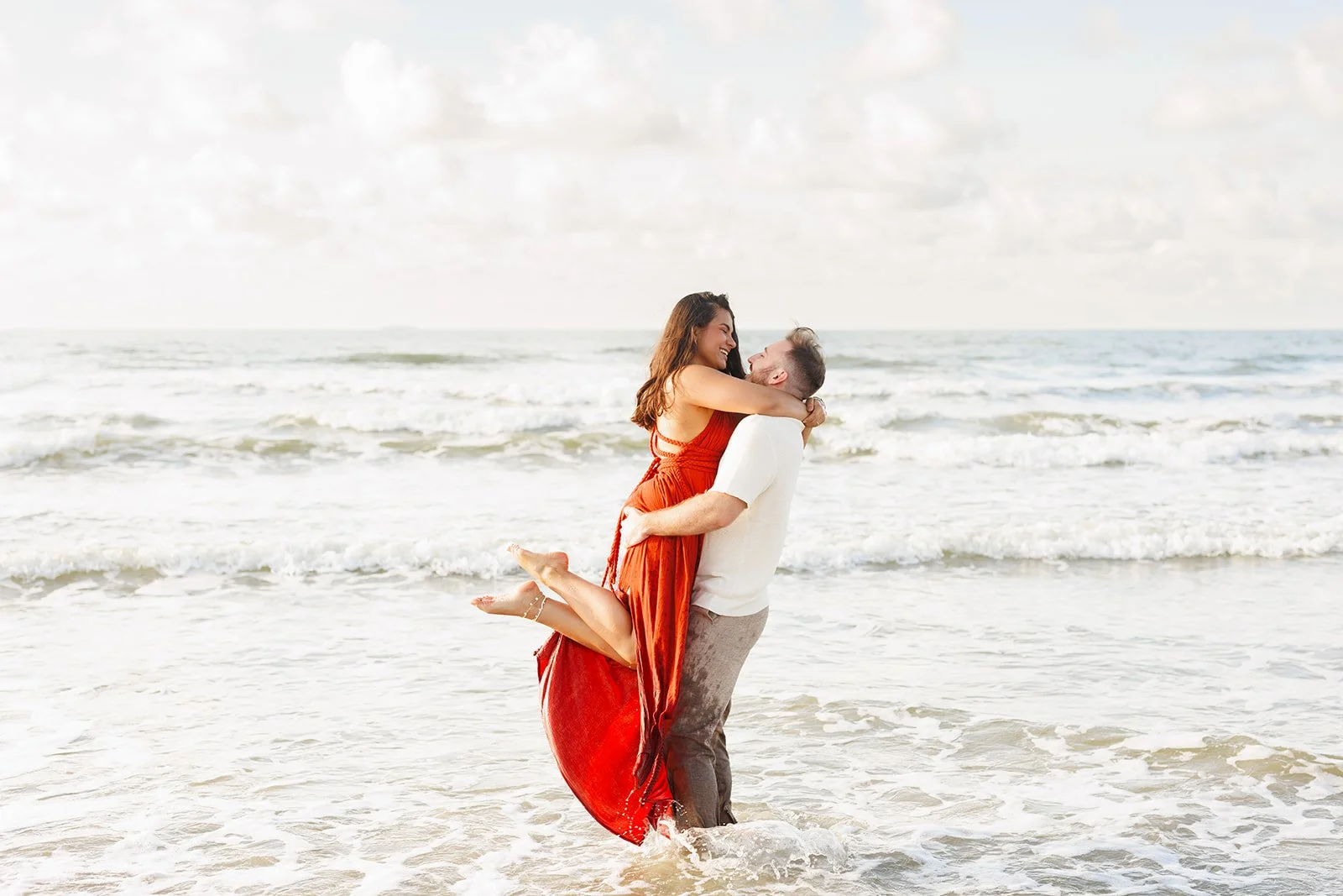 Romantic Galveston beach moment — couple smiling and embracing waist-deep in the ocean — captured by Wild Ivy Creative.