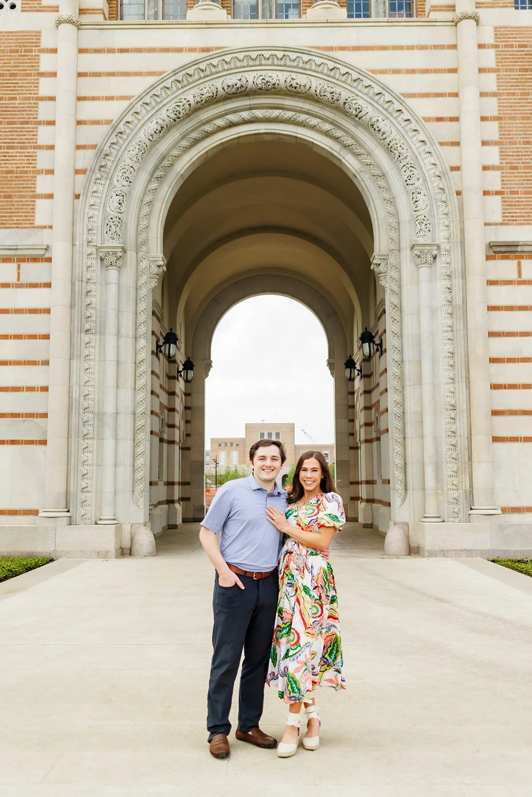 Joyful engagement portrait at a Houston Rice university campus under a decorative stone archway, featuring a colorfully dressed couple — by Wild Ivy Creative.