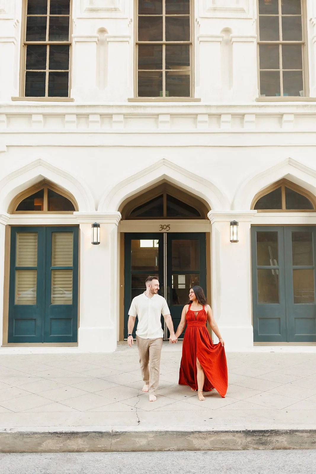 Barefoot engagement session outside a historic Galveston building with arched windows and blue doors — colorful and casual moment captured by Wild Ivy Creative.