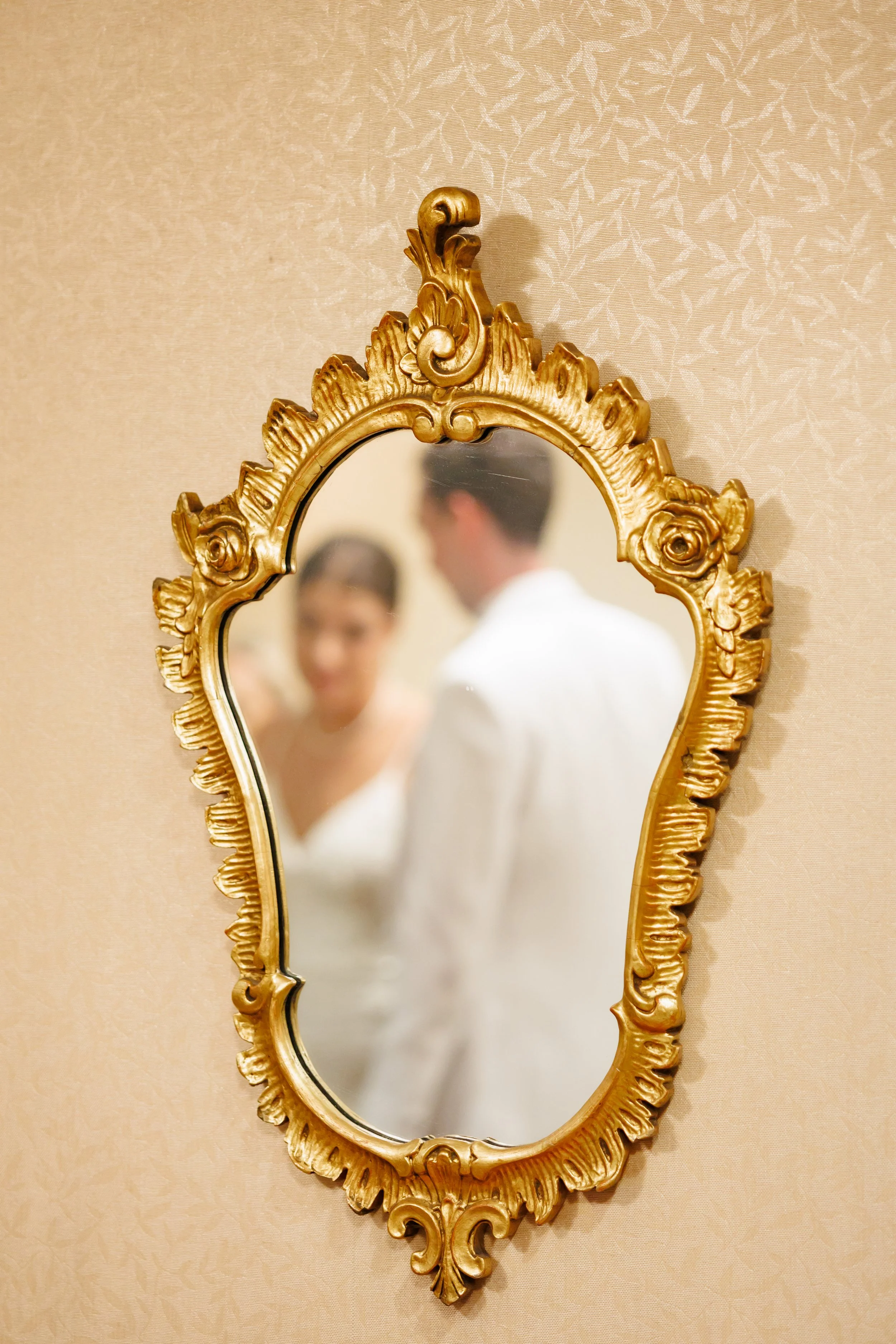 Reflection of a newlywed couple in an ornate gold mirror at a Houston wedding venue, with warm tones and elegant detailing.