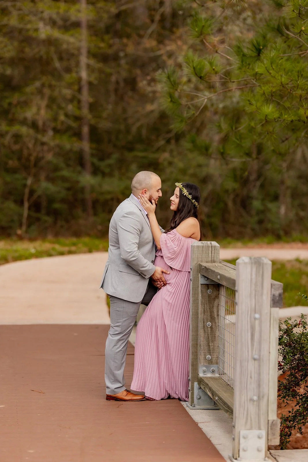 Forest maternity session on a wooden bridge with a couple in romantic attire, captured by Wild Ivy Creative in The Woodlands, Texas.