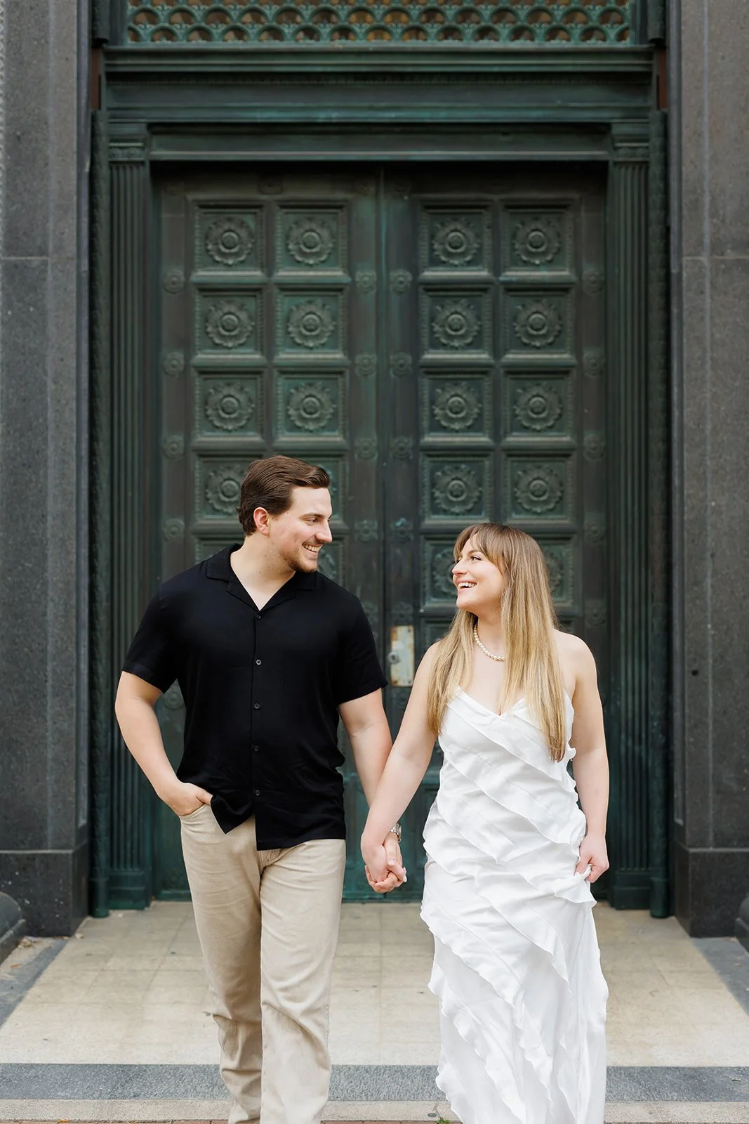 Romantic engagement session in Houston with a couple walking hand in hand in front of a grand green door — captured by Wild Ivy Creative.
