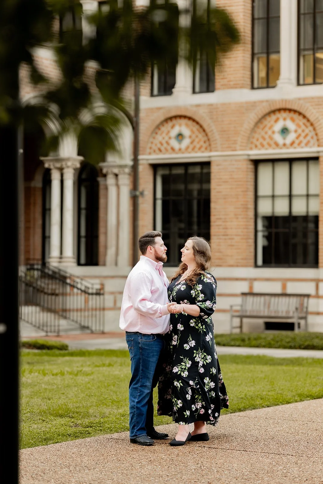 Candid outdoor engagement session in Houston with a couple in front of a historic brick building at Rice University with arched windows — photographed by Wild Ivy Creative.