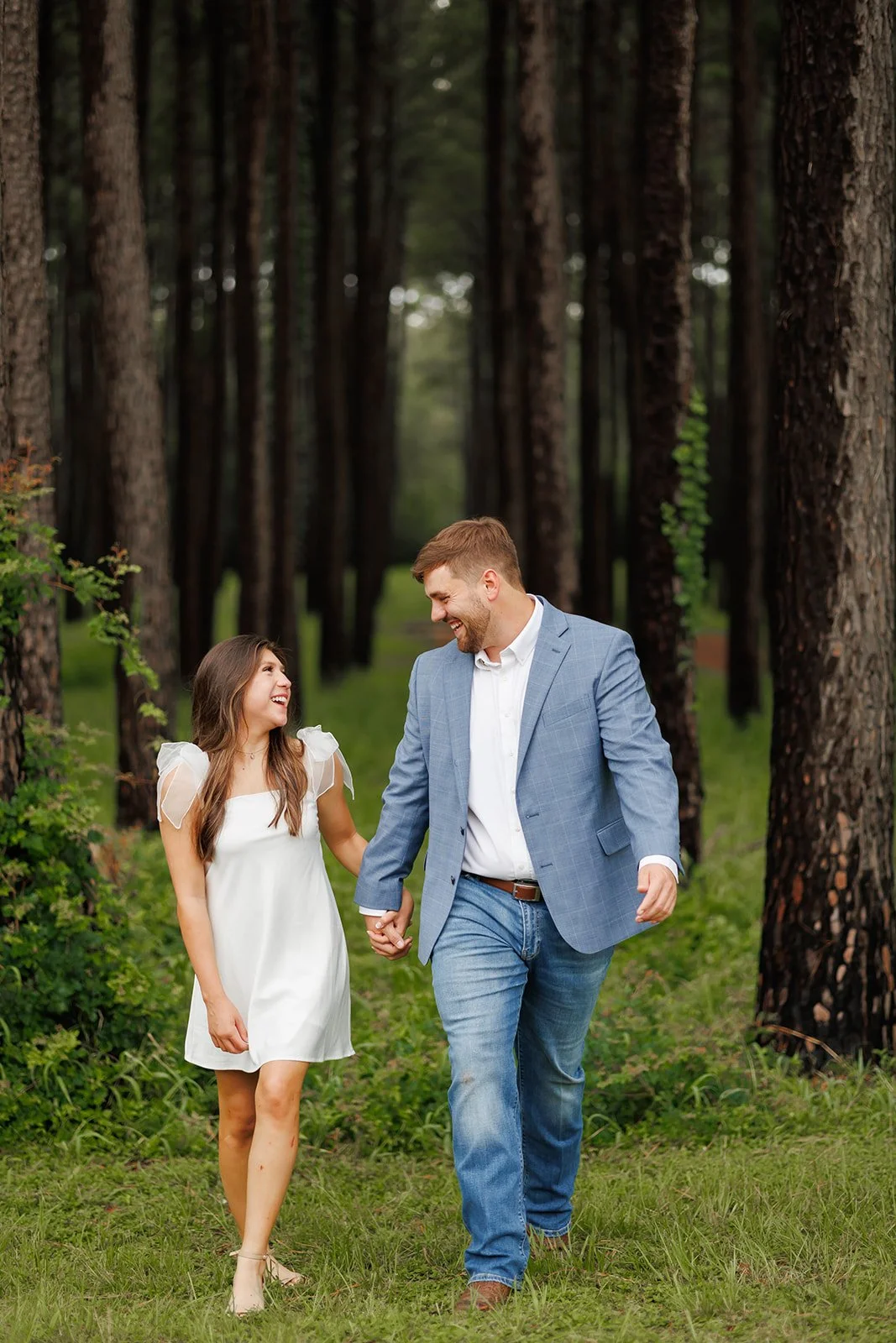 Forest engagement session in The Woodlands featuring a young couple walking hand-in-hand among tall trees and greenery.