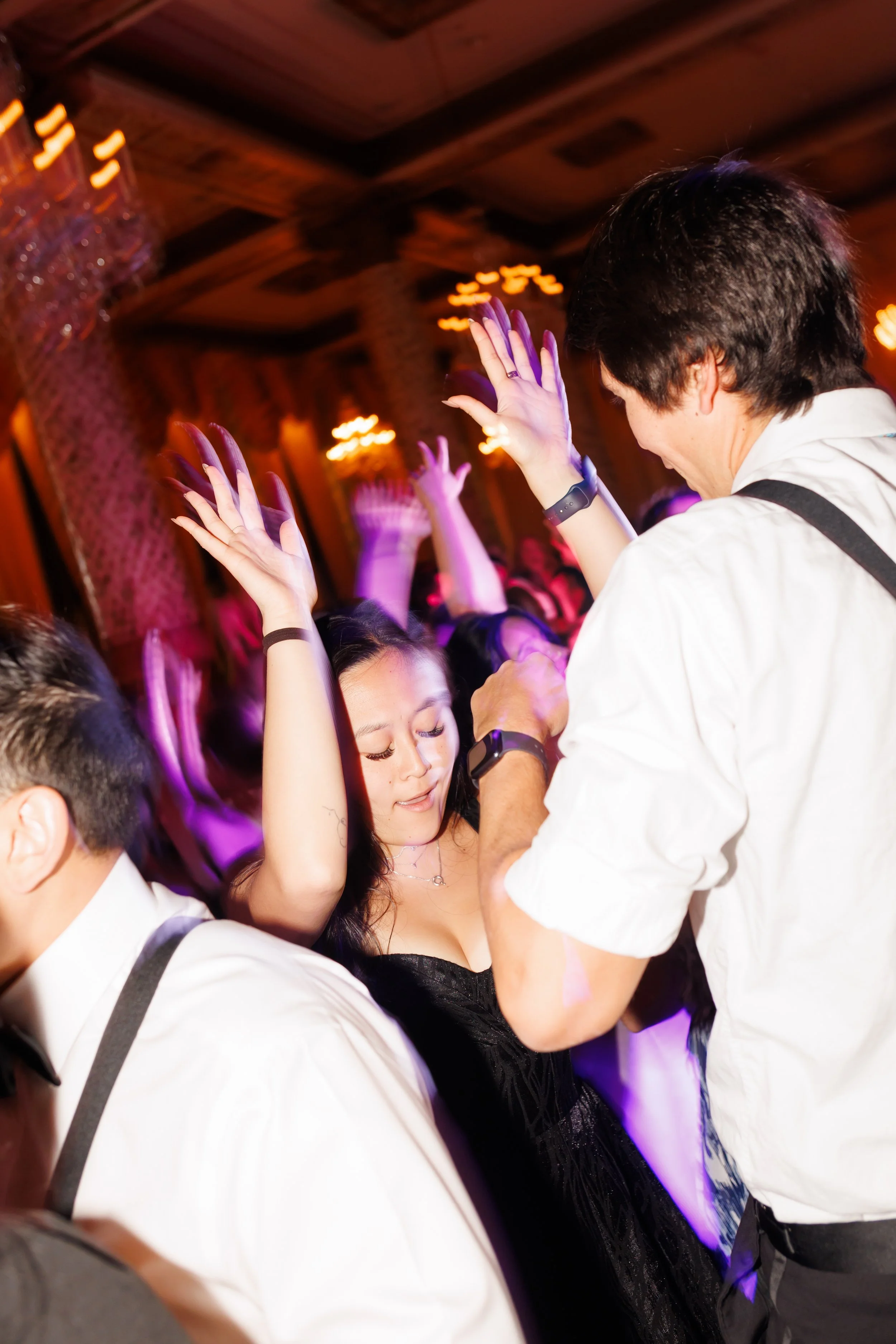 Guests dancing at a lively Houston wedding party, with a woman in a black dress raising her arms in joy, eyes closed, and music filling the air.