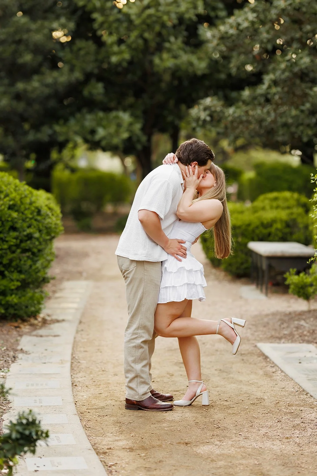 Intimate garden kiss during a Houston engagement session — couple styled in neutrals surrounded by lush greenery — Wild Ivy Creative.