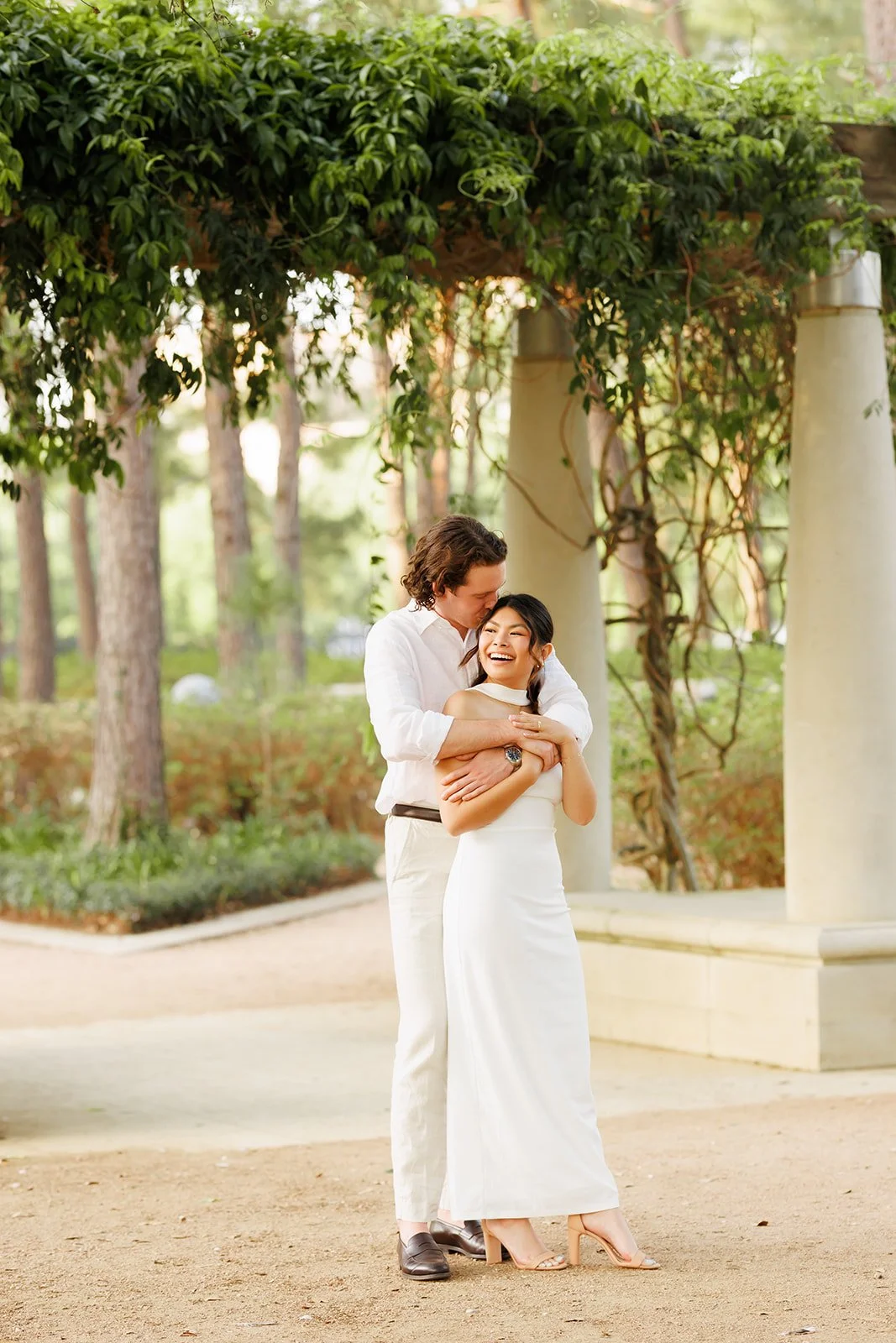 A joyful couple embracing outdoors near columns with greenery in the background.