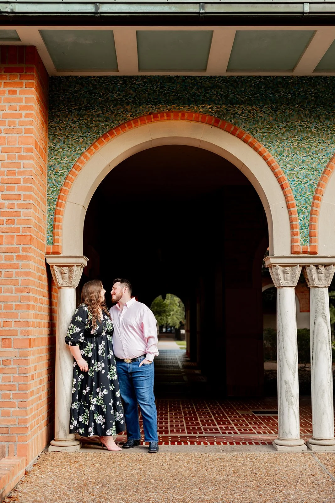Houston engagement photo under a brick-and-tile archway at Rice University, as a couple shares an intimate glance — captured by Wild Ivy Creative.