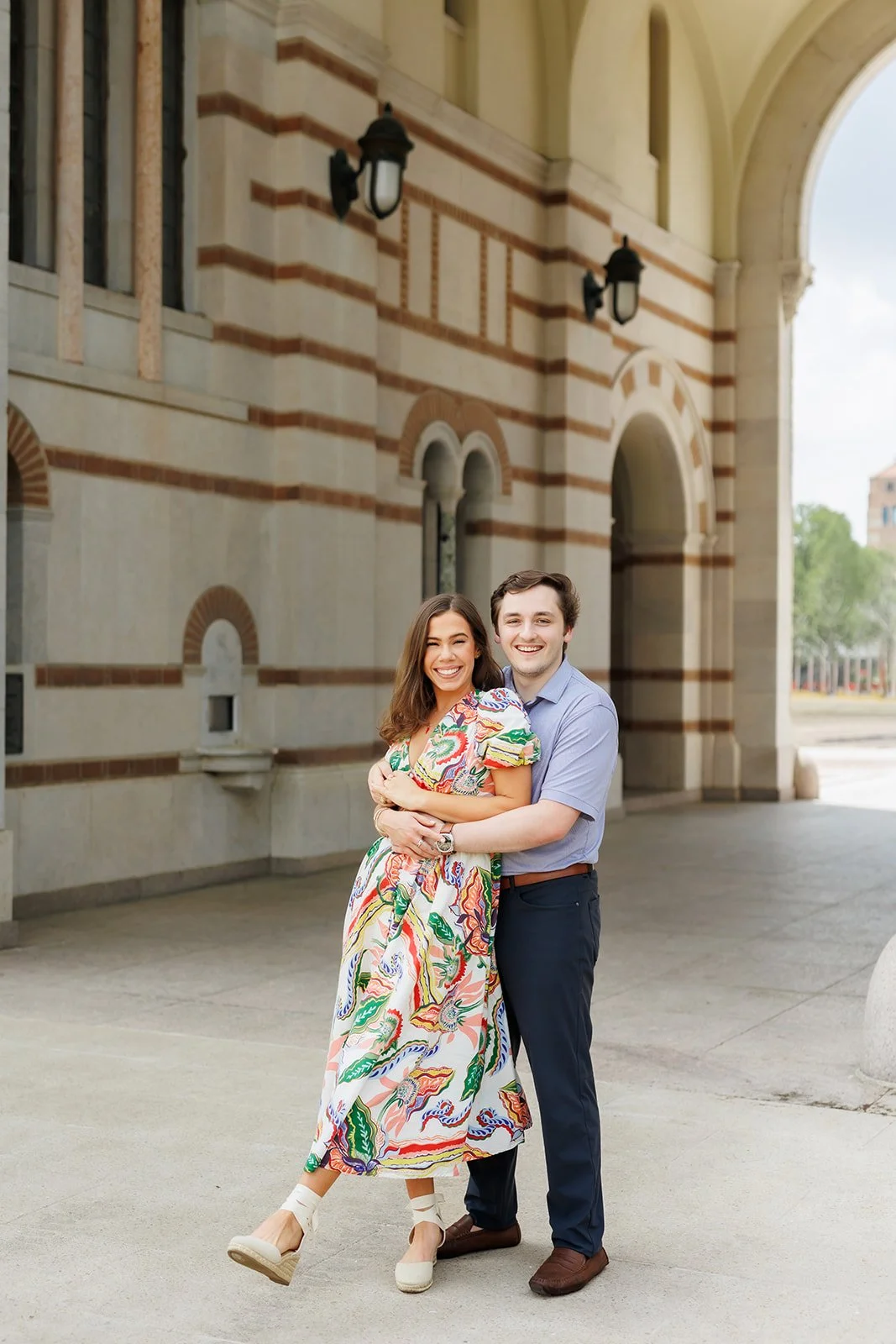Outdoor engagement photo of a happy couple in front of arched architecture in Houston at Rice University, styled in light and colorful outfits — Wild Ivy Creative.