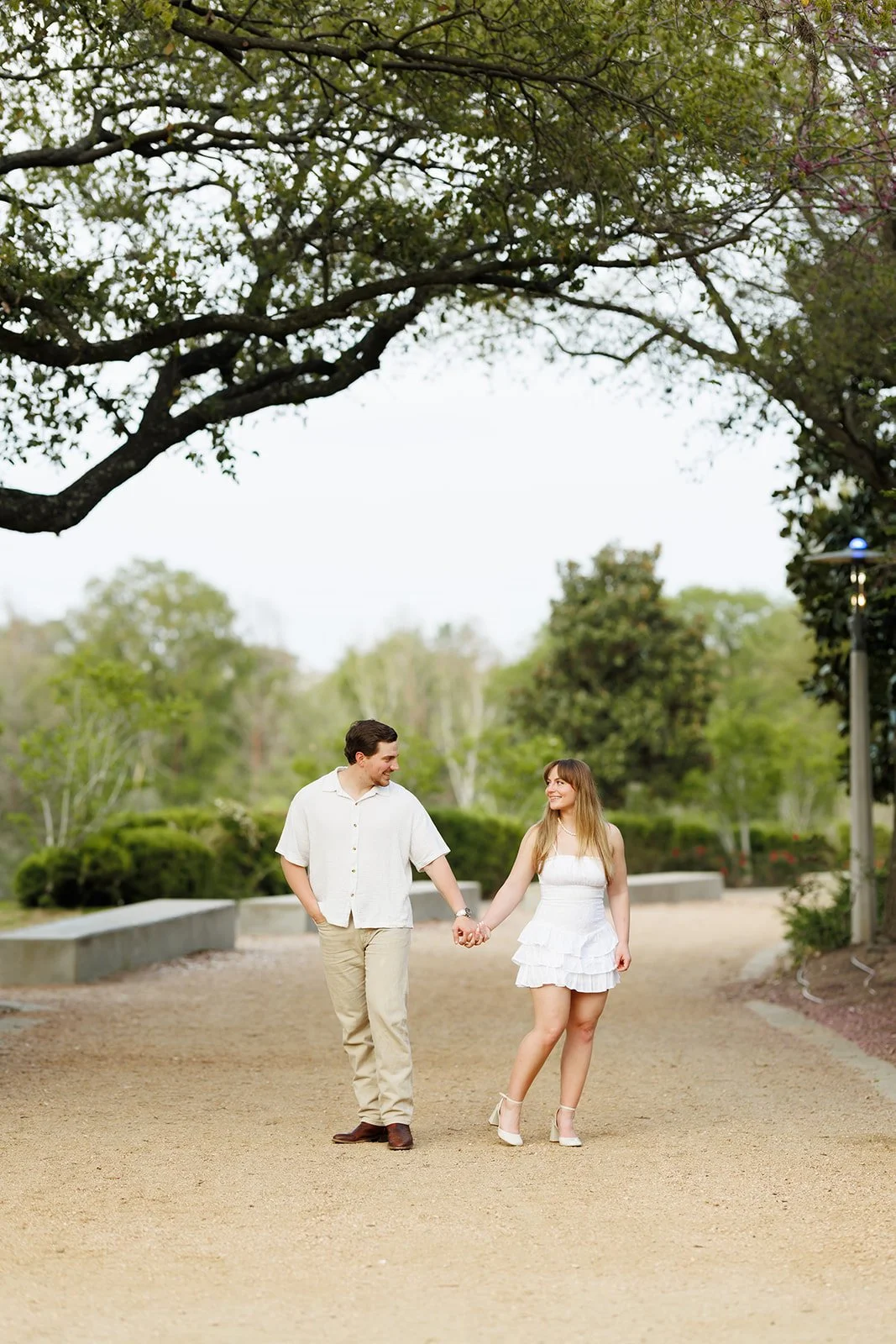 Outdoor engagement session in a park near Downtown Houston— couple walking hand-in-hand through a lush green park — by Wild Ivy Creative.