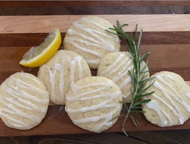 six rosemary lemon cookies with drizzled lemon icing shown with a fresh lemon slice and sprig of rosemary