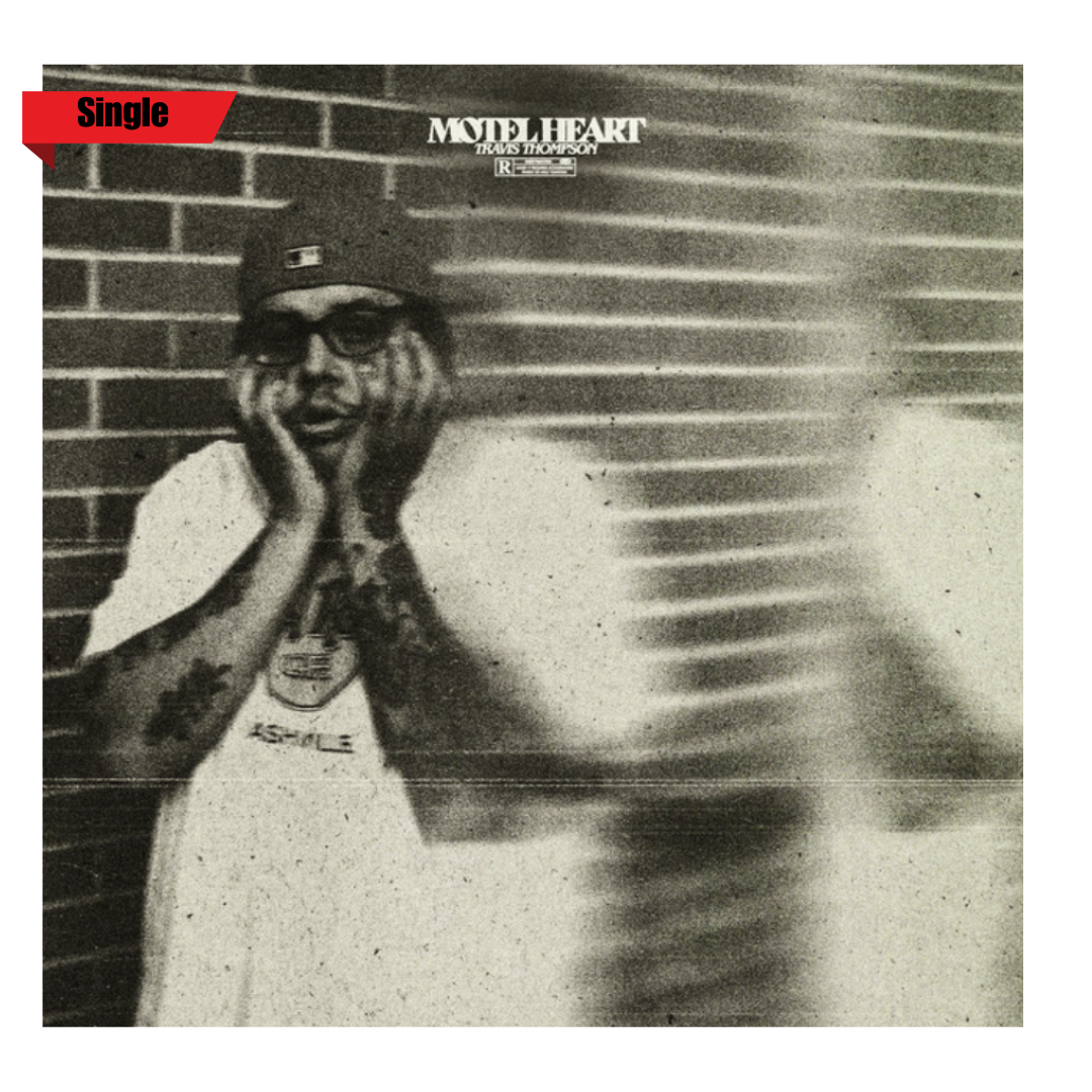 Black and white photo of a person with long hair, wearing glasses, and tattoos on their arms, standing against a brick wall. They have a surprised or excited expression with hands on their face. There is a poster or sign above them for "Motel Heart" with a smaller text "Travels Thompson" and a red banner in the top left corner with the word "Single."