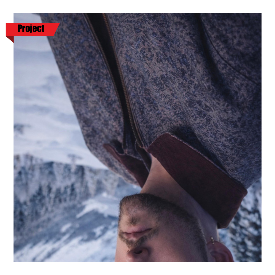 Man with a beard in winter clothing outdoors in snowy mountain landscape, taking a selfie.