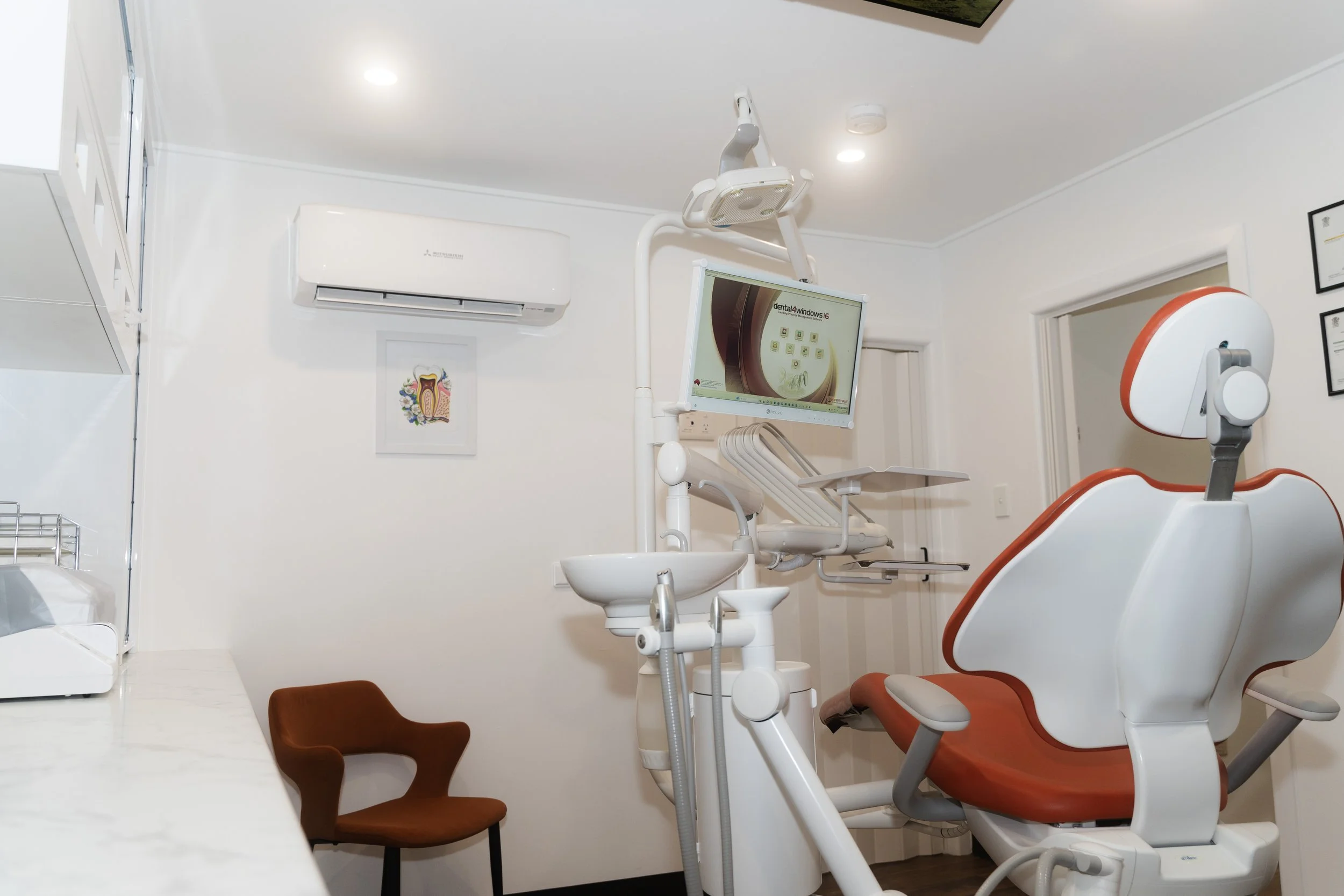Dental examination room with dental chair, monitor, dental equipment, and a small brown chair.