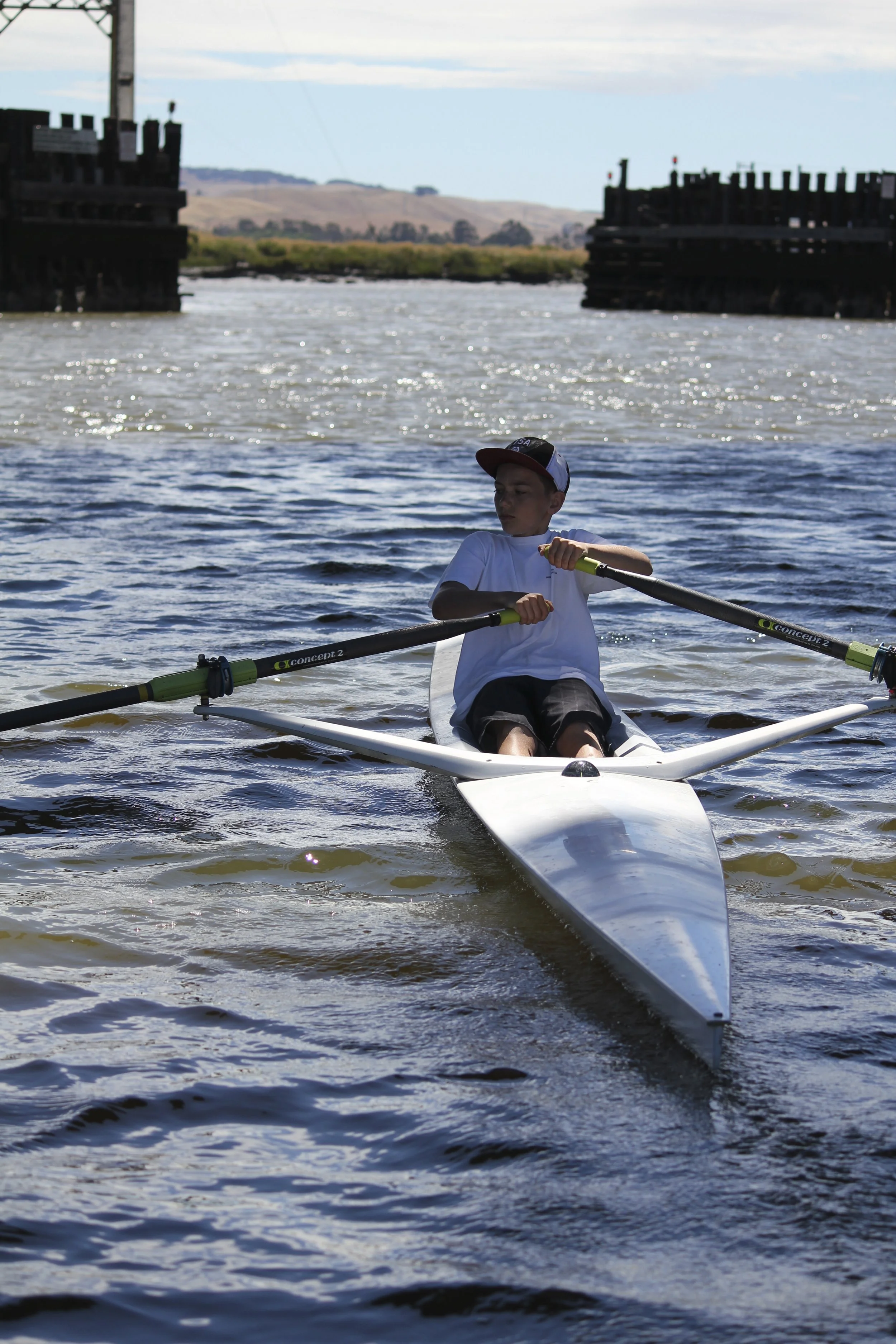 Floathouse Summer Camper tries sculling, at Haystack Landing. Prior to the 2015 construction of the SMART RR bridge and new highway bridge. (2014)