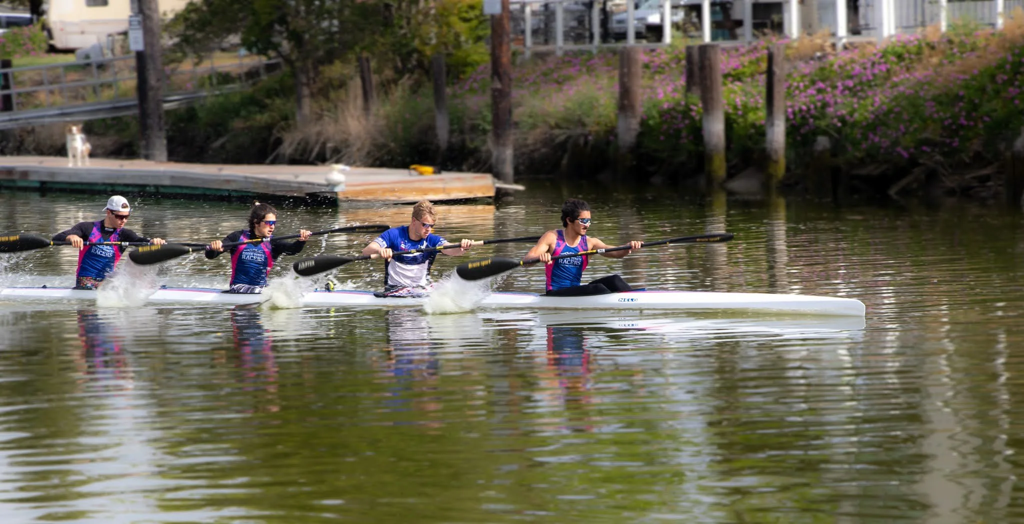 A four-person kayak speeds past Foundry Wharf, skillfully paddled by members of the River Town Racers sprint kayak team , founded in Petaluma and flourishing and medaling nationally and internationally.  (2021. Photo by Marcus Moore) 