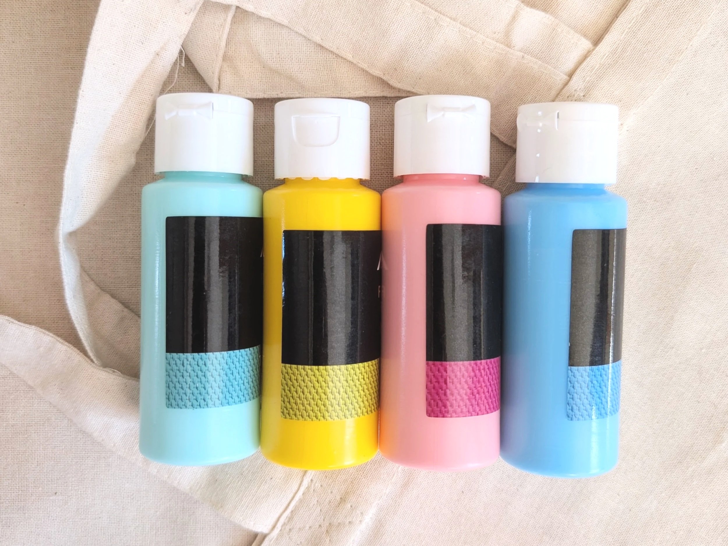 Pink, yellow, blue and turquoise fabric paints. Laying on top of blank tote bags..