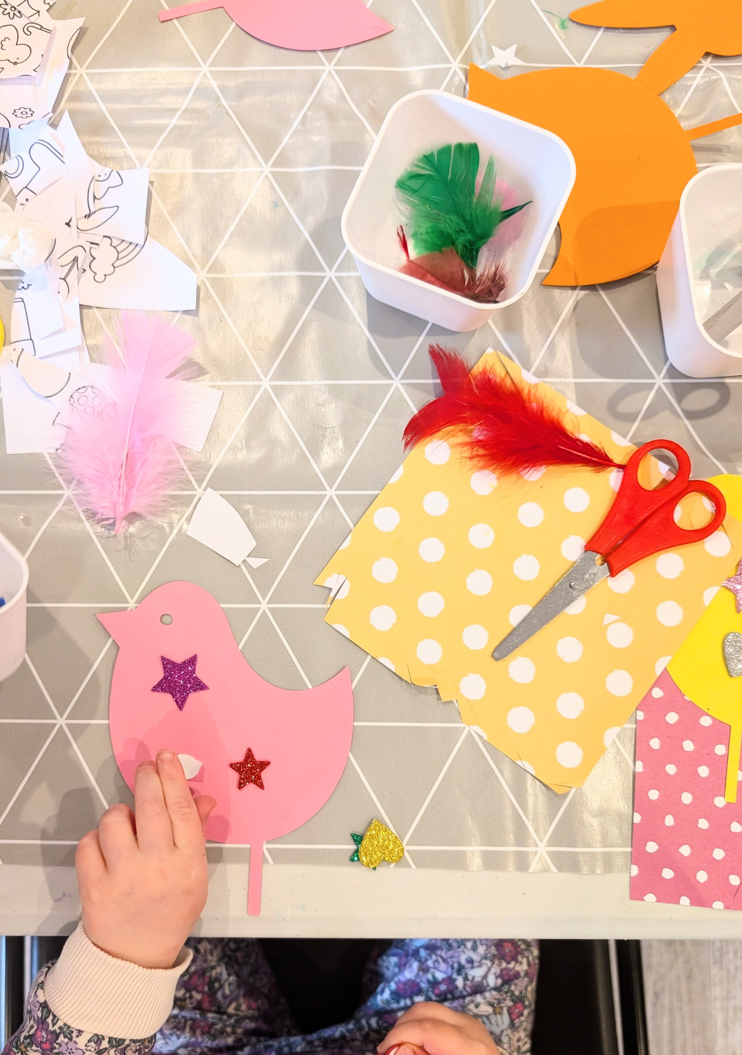A selection of craft materials, being used by a girl to decorate a card bird.
