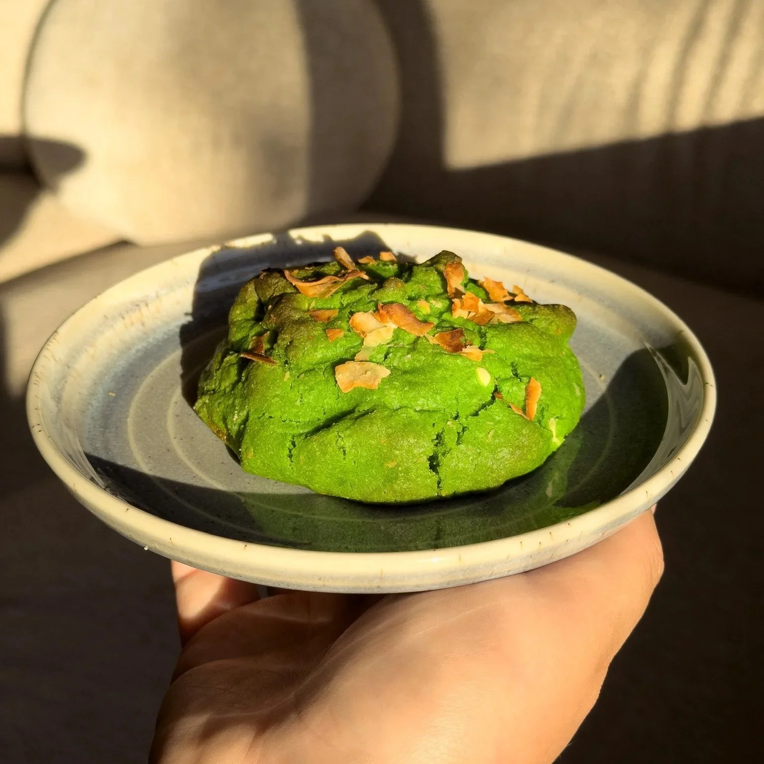 A green matcha-flavored dessert topped with toasted coconut flakes served in a black and white ceramic bowl.