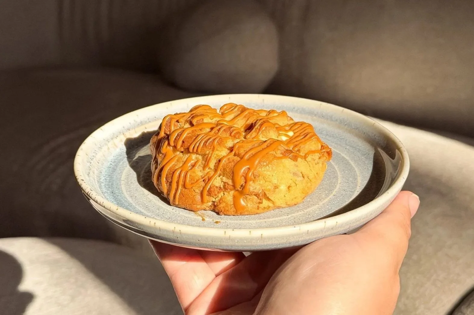 A hand holding a small ceramic plate with a baked good topped with biscoff drizzle.