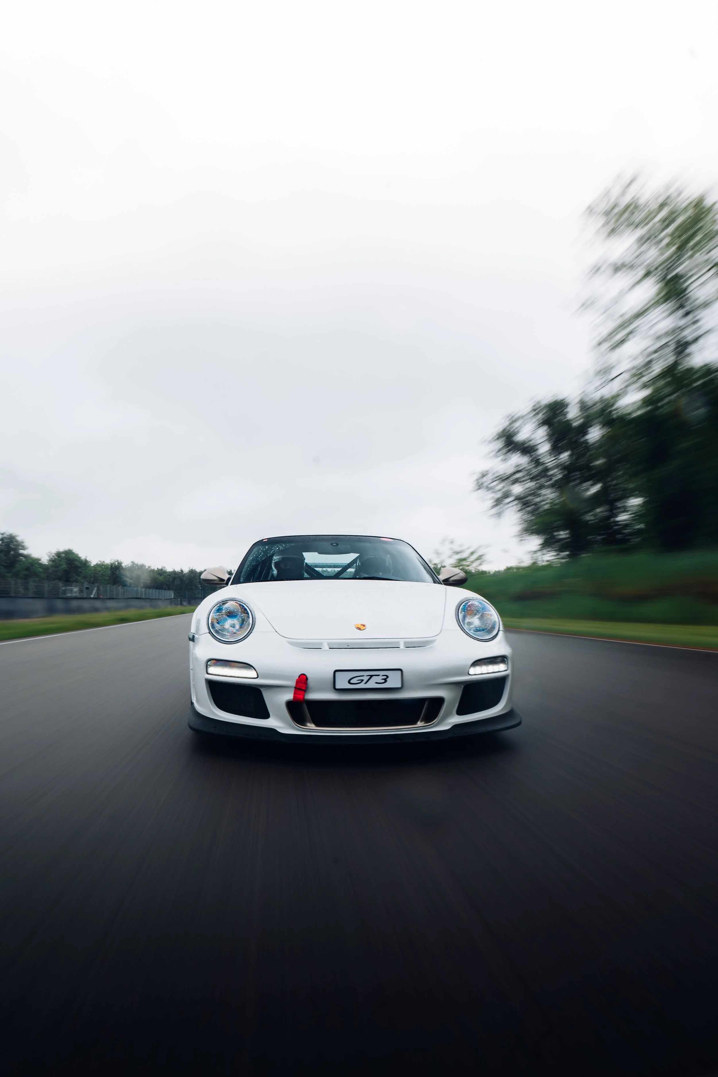 Weiße Porsche GT3 auf einer Rennstrecke bei leicht bewölktem Himmel, bewegungsunschärfe nach vorne gerichtet.